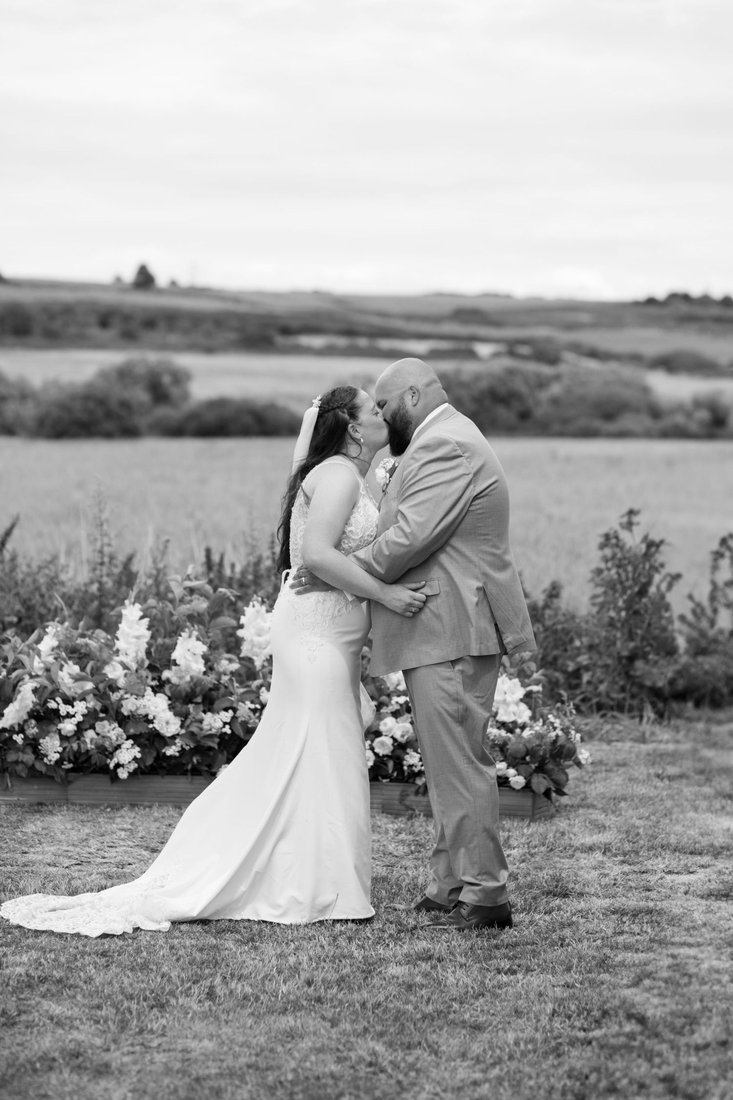 Bride and Groom share their first kiss during their outdoor ceremony at Weymouth and Portland Rugby Club. Photo in black and white