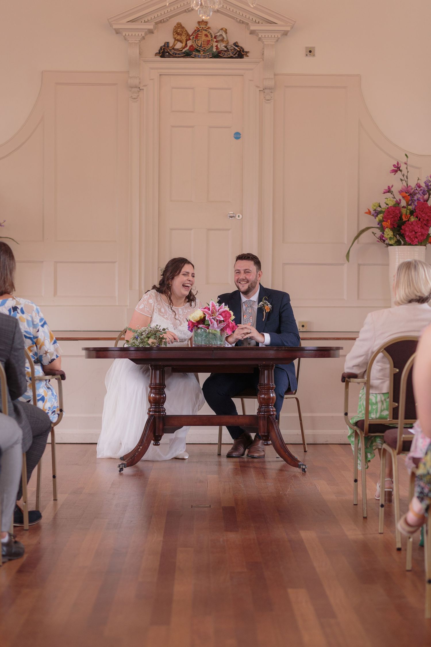 Bride and groom laugh together as they sit at a table to sign their marriage certificate