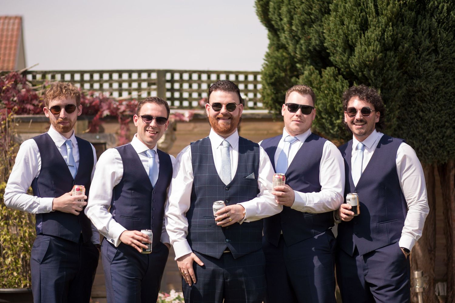 Groom and his four groomsmen in matching navy blue suits posing for a group photo in the garden before the ceremony.