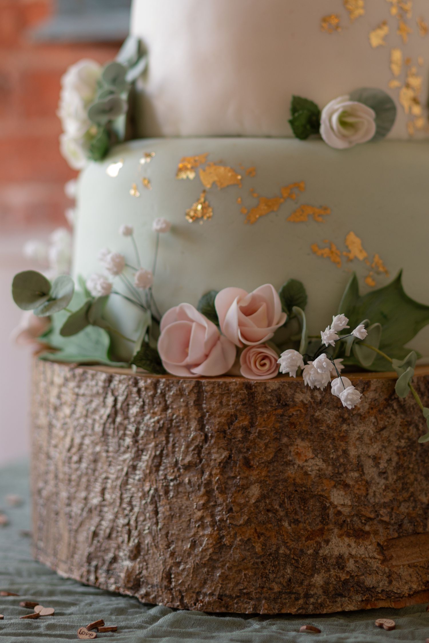 Close up details of a wedding cake. Pink and green tiers, fondant roses and leaves, and placed on top of a slice of a log.