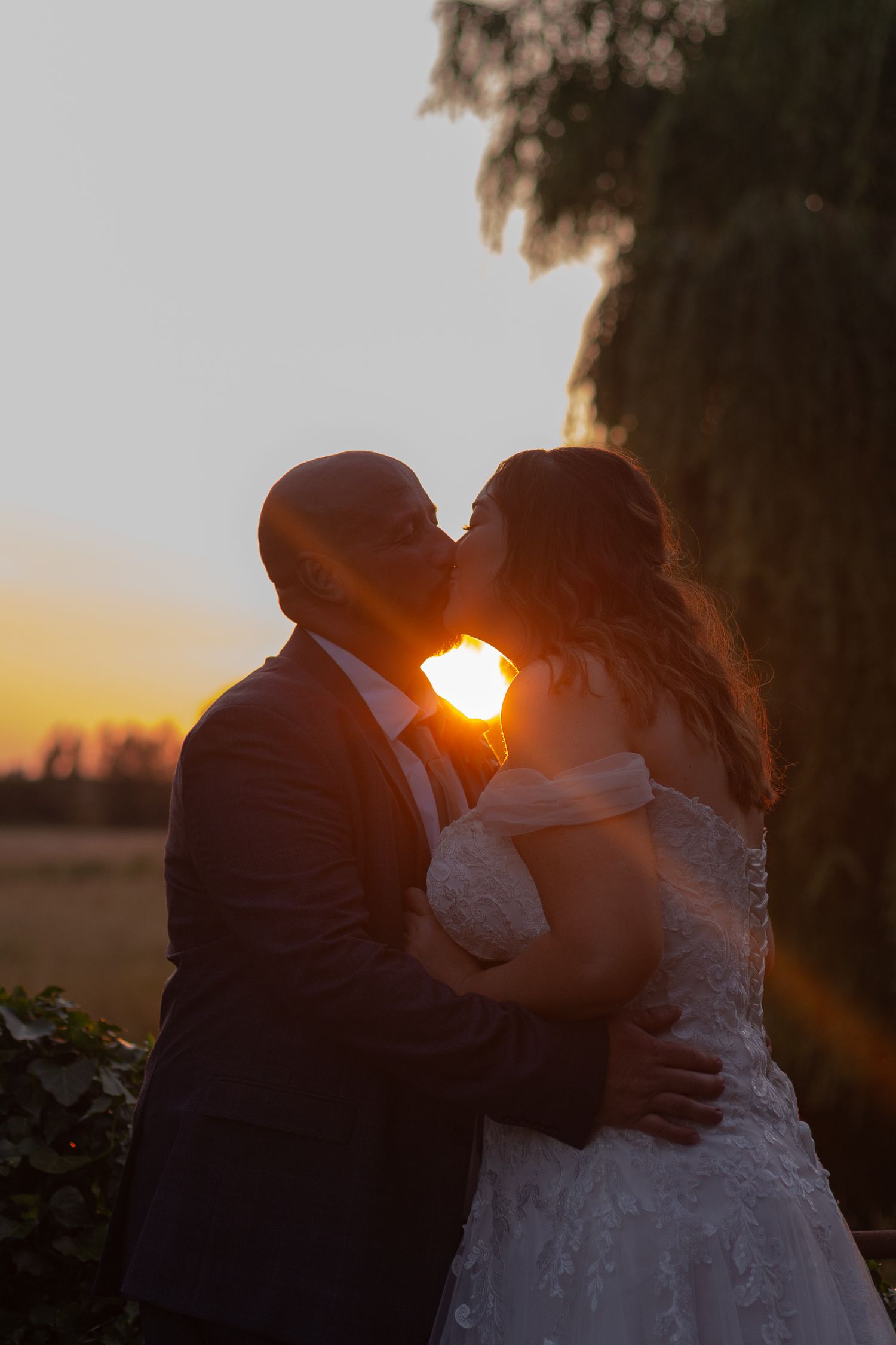 Bride and Groom share a kiss during sunset. Silhouetted, with the late evening sun shining between them