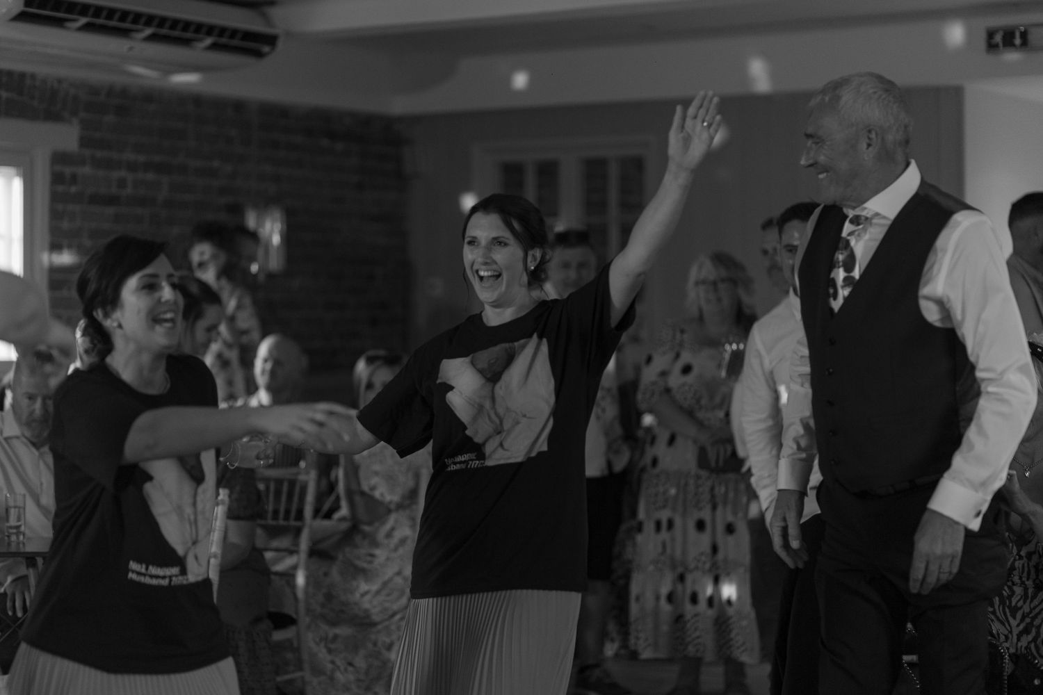 Wedding guests laughing with their arms outstretched as they make their way onto the dance floor
