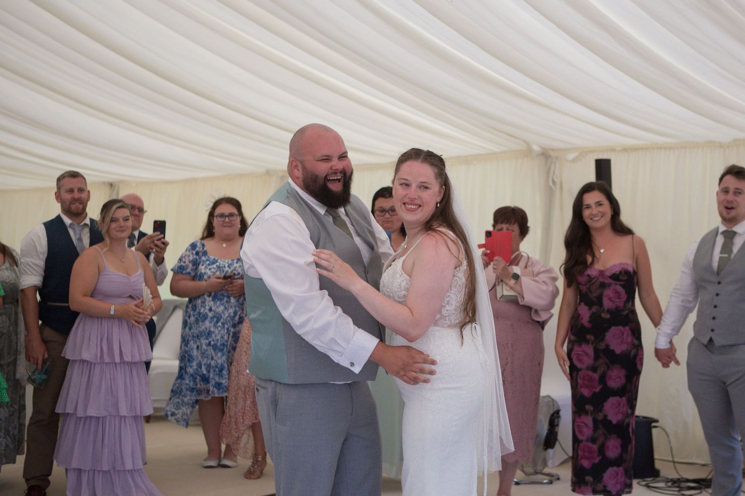 Bride and Groom laugh at their guests singing (offscreen) during their first dance.