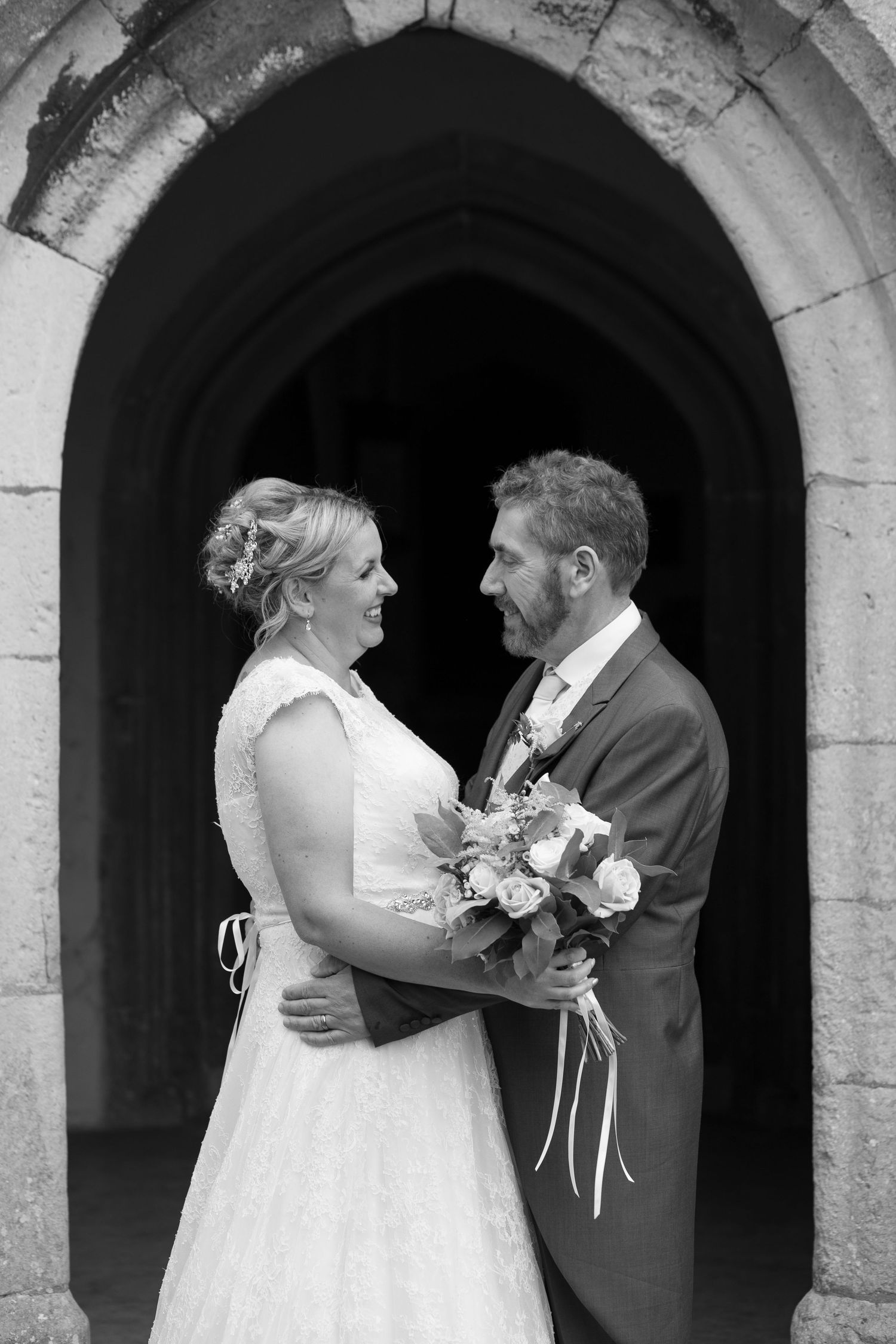 Bride and Groom pose chest to chest, smiling, for portraits in the church doorway