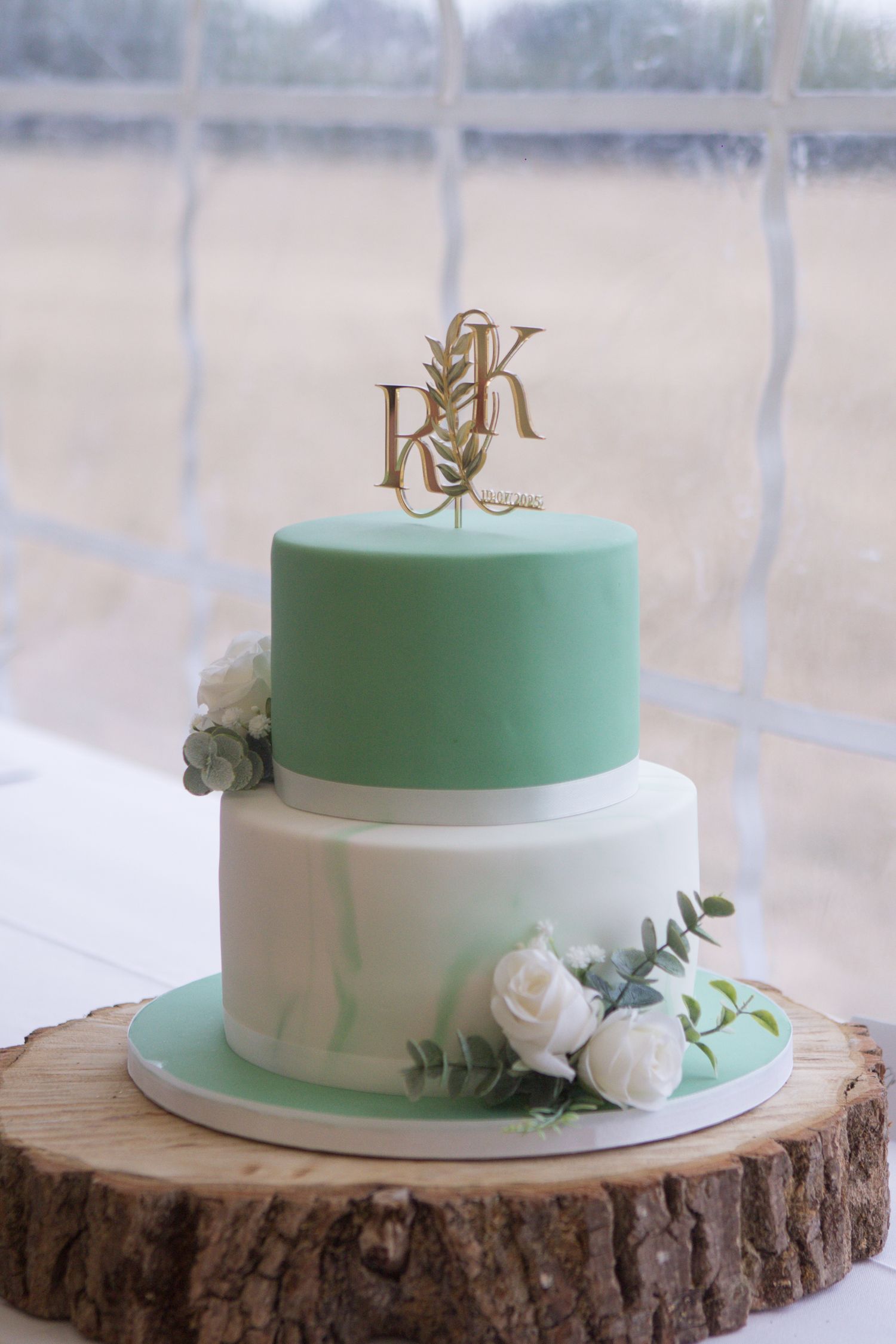 A white and green wedding cake, placed on top of a wooden log cake stand. With a Rugby ball shaped cake topped with their initials.