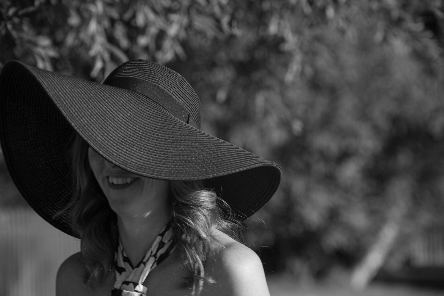 Black and white photo of a female wedding guest, her face half obscured by a wide brimmed sun hat