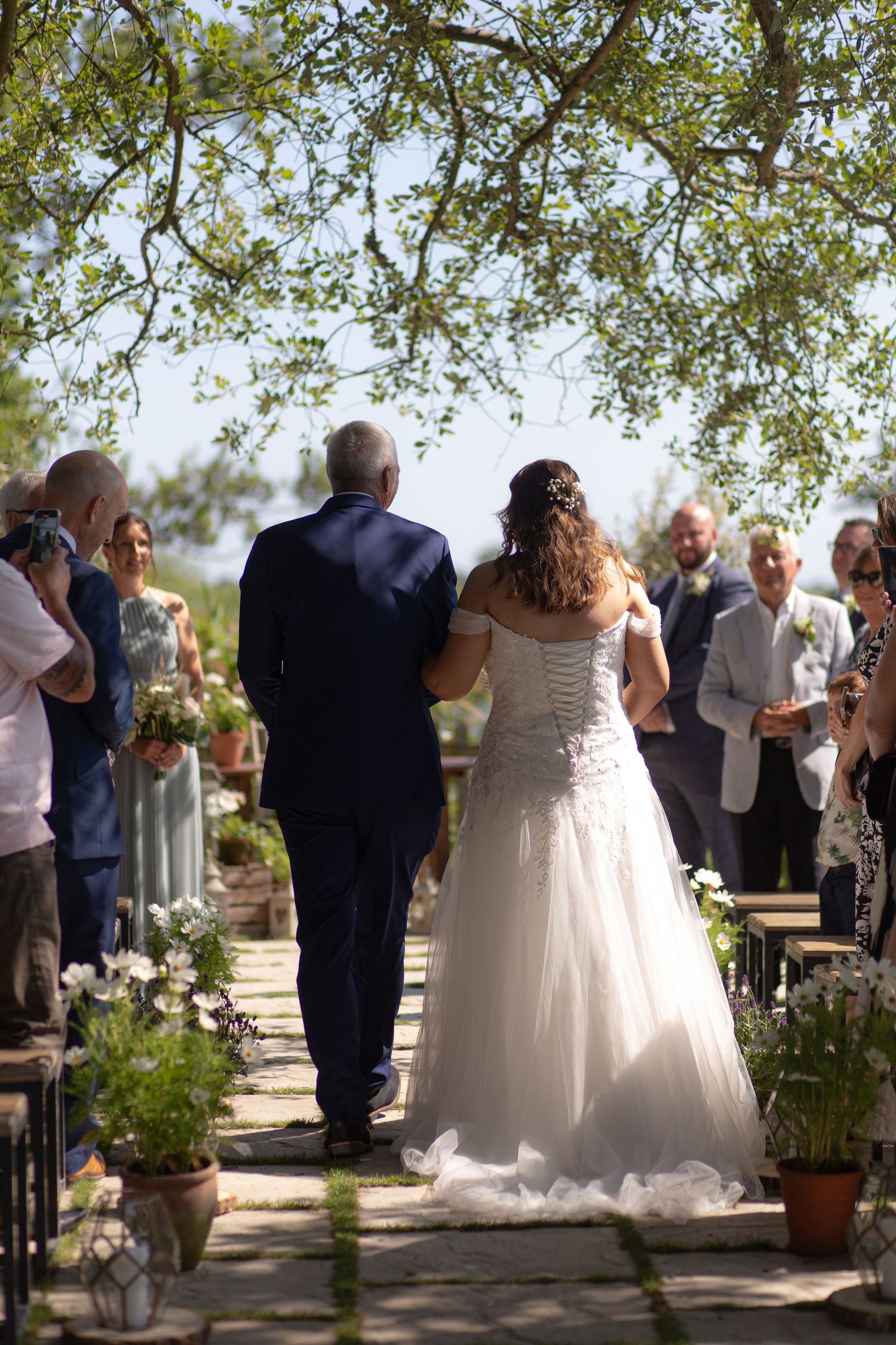 Bride and her father walk down the aisle at Sopley Mill, under the shade of a tree