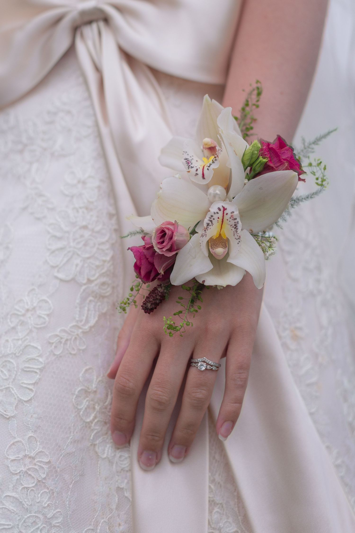 A close up photo of a brides corsage, tied around her wrist with ribbon. A beautiful collection of white and red flowers.