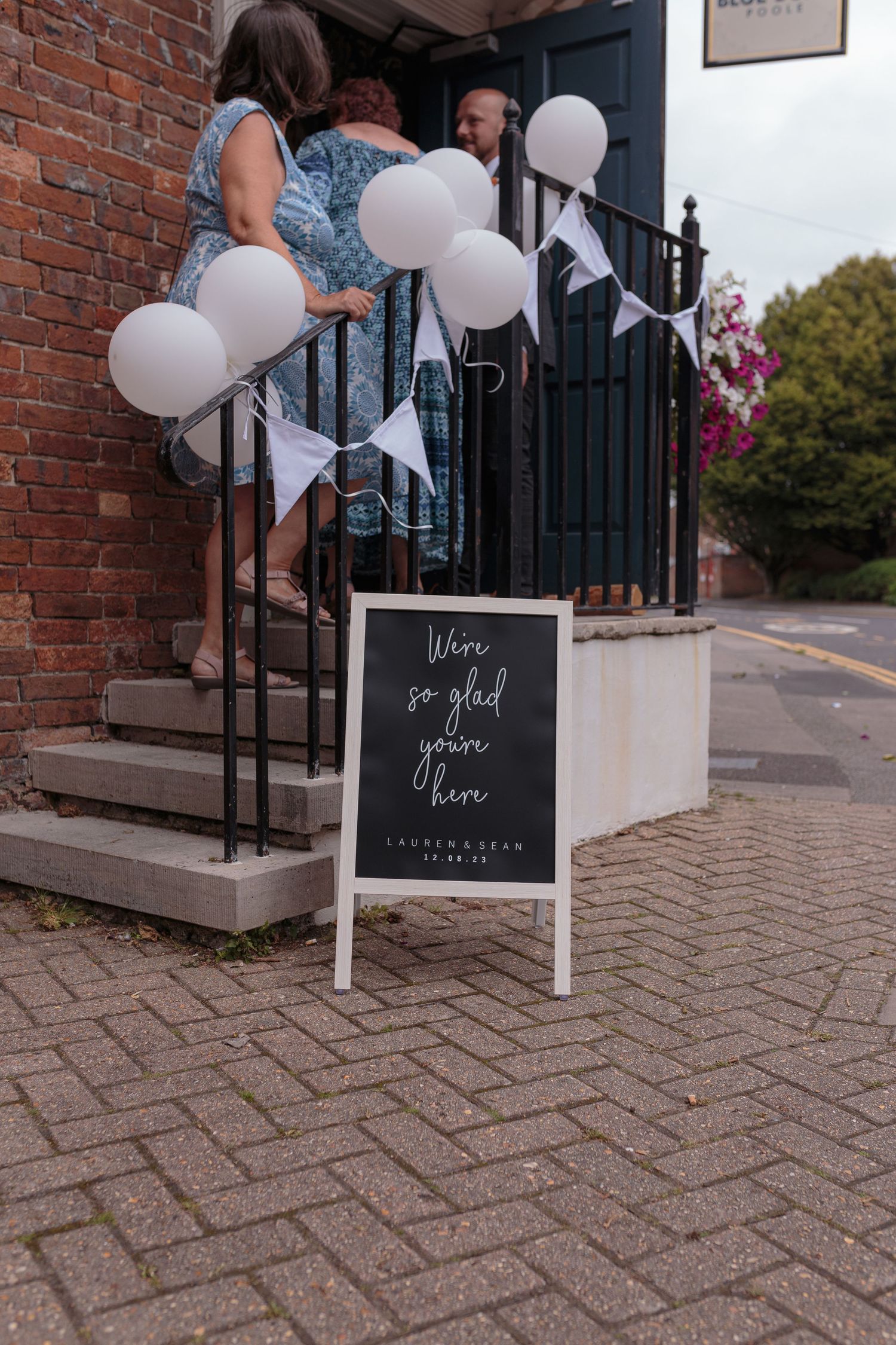 A small wedding welcome sign sits at the bottom of some stairs, its railings covered in balloons