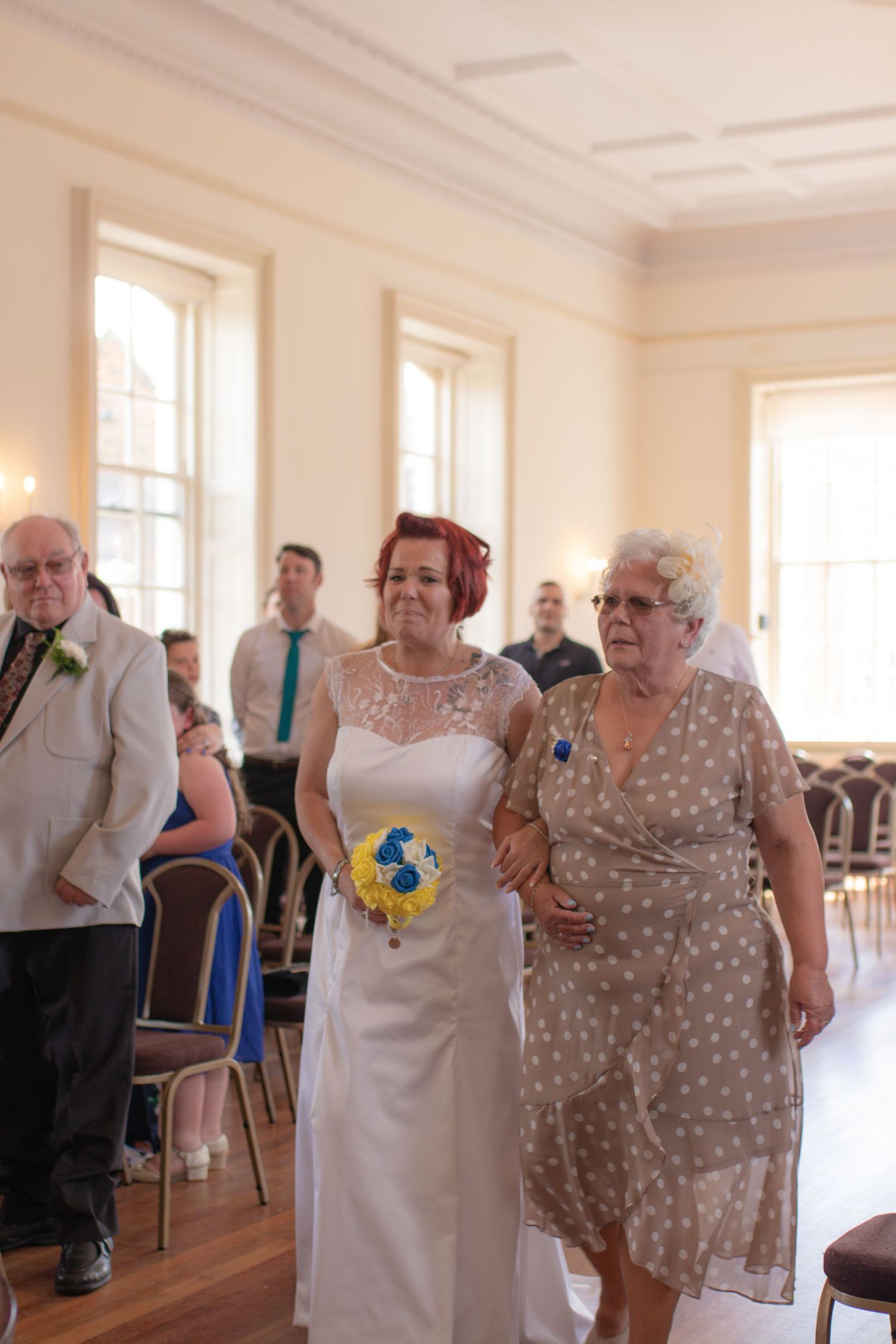 Emotional bride and her mother walking down the aisle at the start of wedding ceremony at Poole Guildhall.