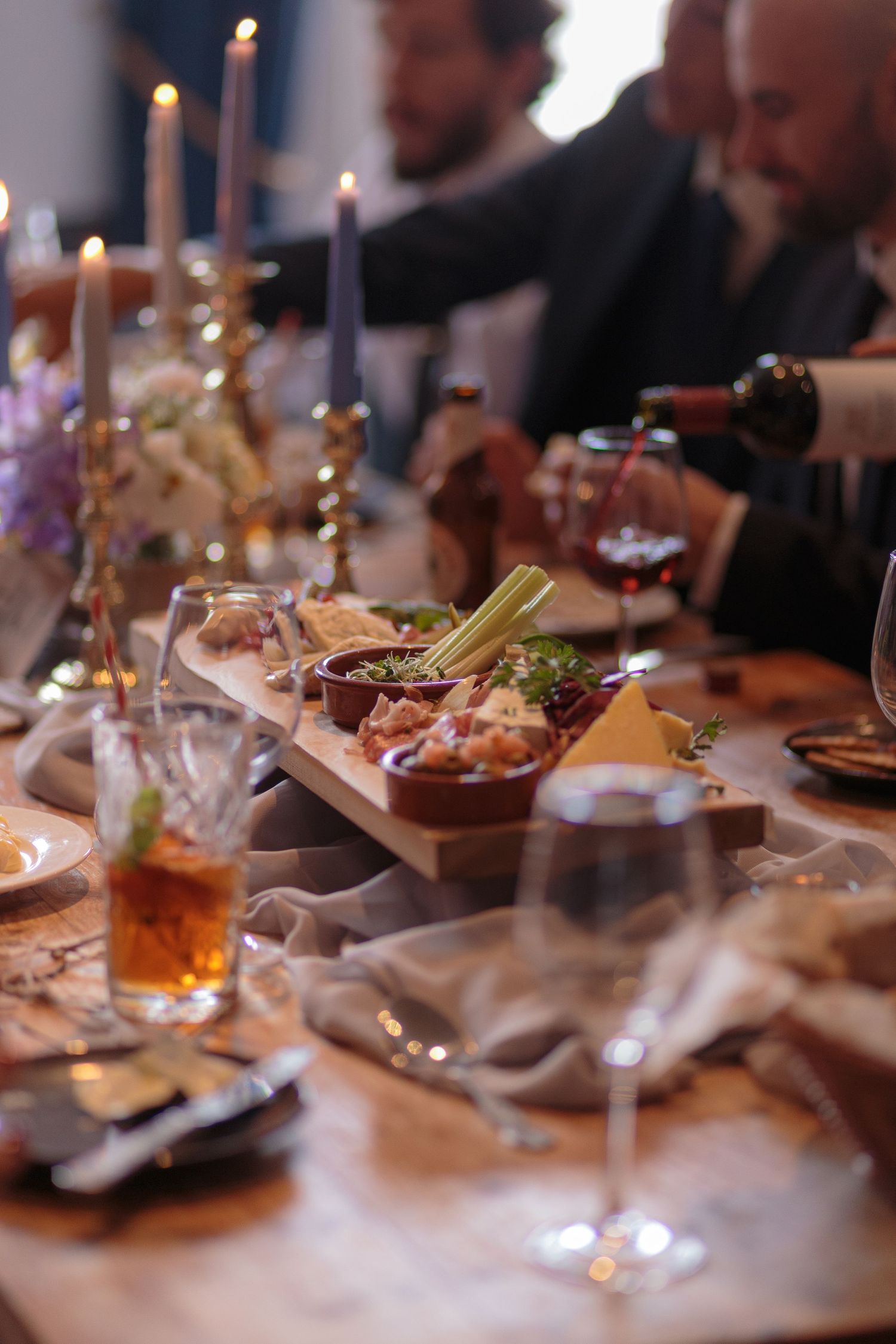 Close up on a wedding breakfast table. Drinks being poured all around, candles burning away and a charcuterie board in the centre