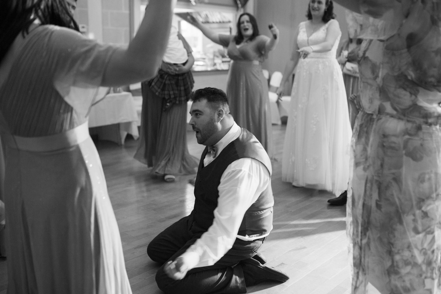 A groomsmen sliding on his knees in the middle of a reception dance floor dance circle. Other participants cheering in the background