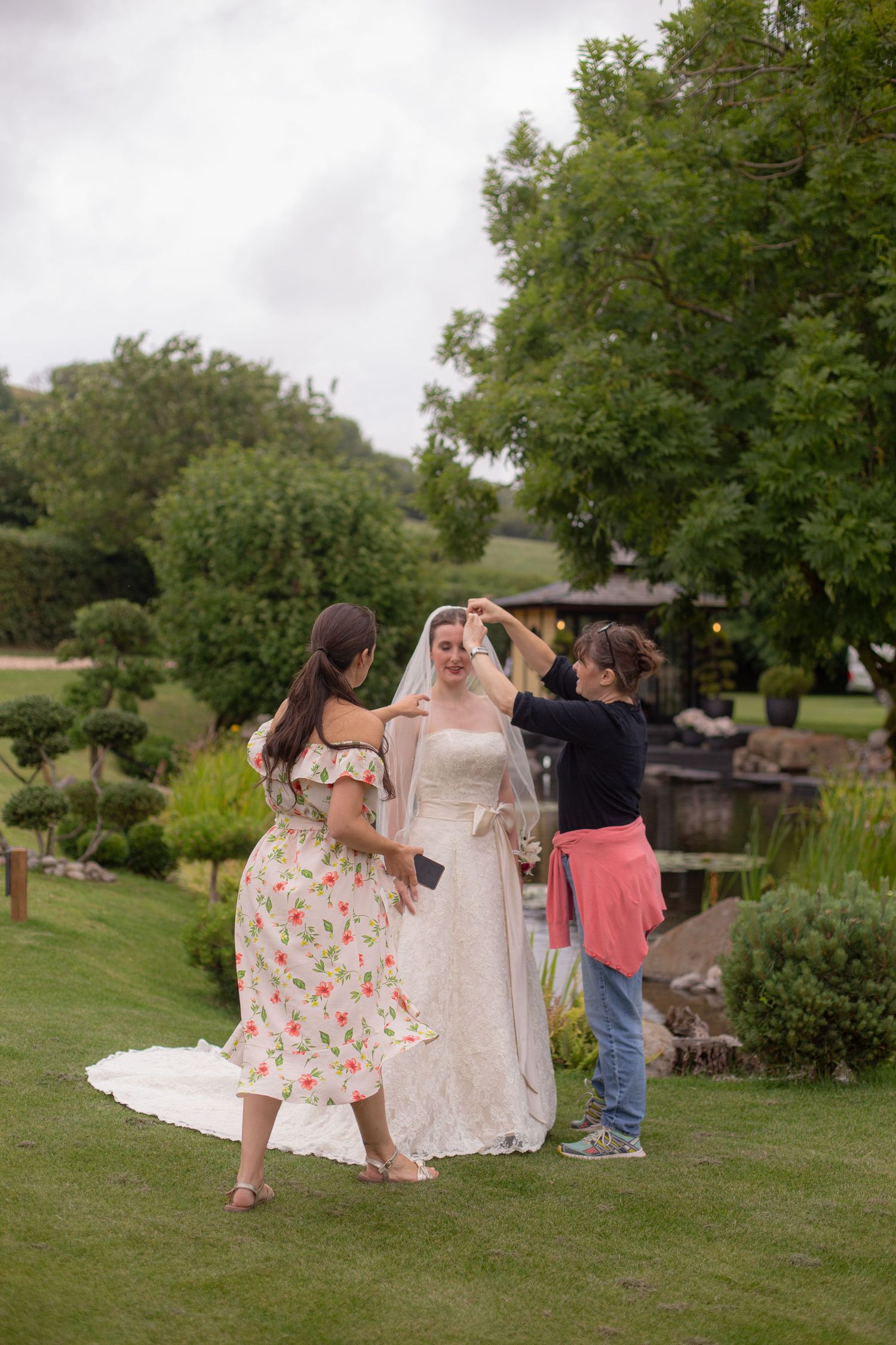 A bride ready to pose for portraits as two women help adjust her dress and veil for the photos.