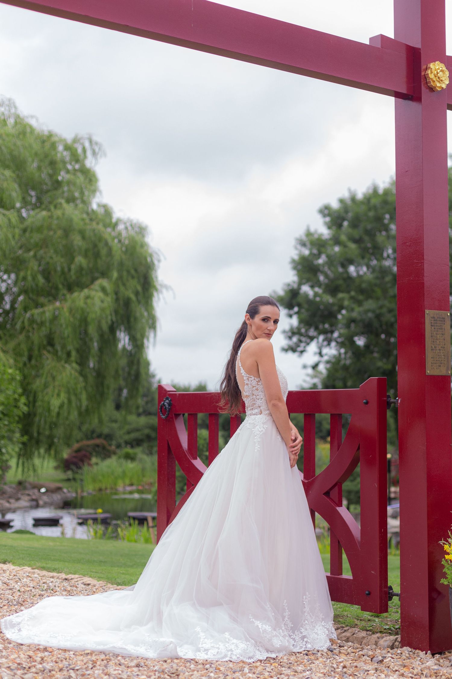 A bride poses for a photo in an elegant ballgown next to the red posts of a Japanese themed gate.