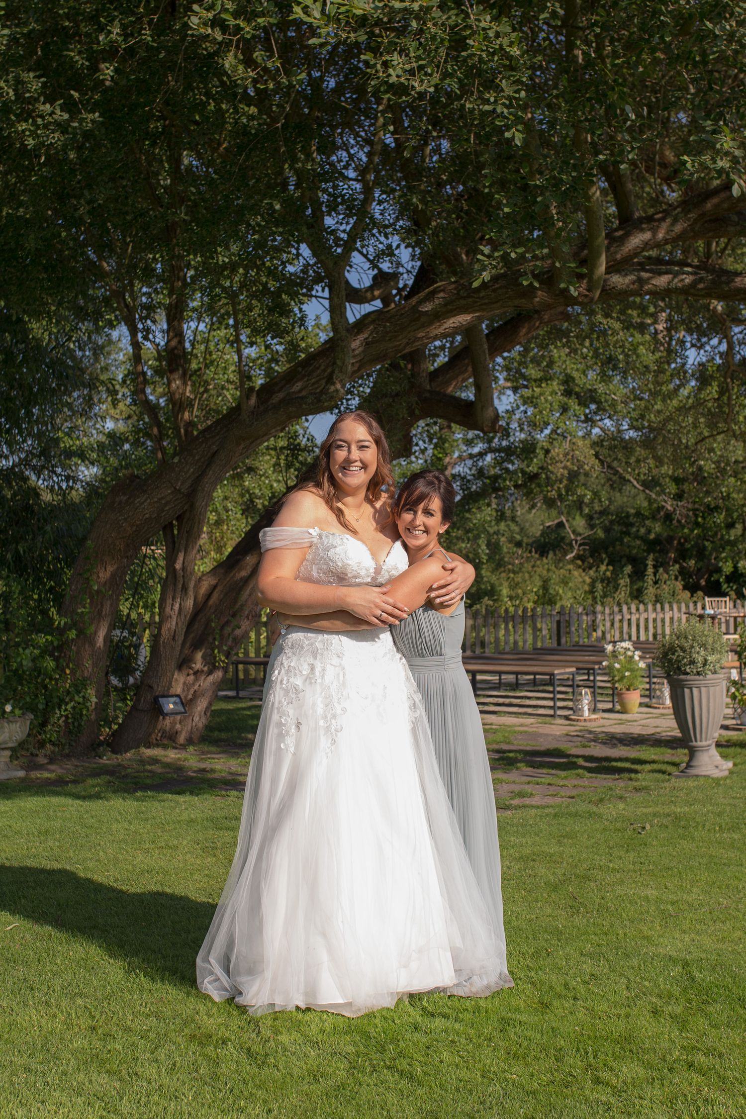 Bride wrapped in a hug with her maid of honour in the grounds of sopley mill