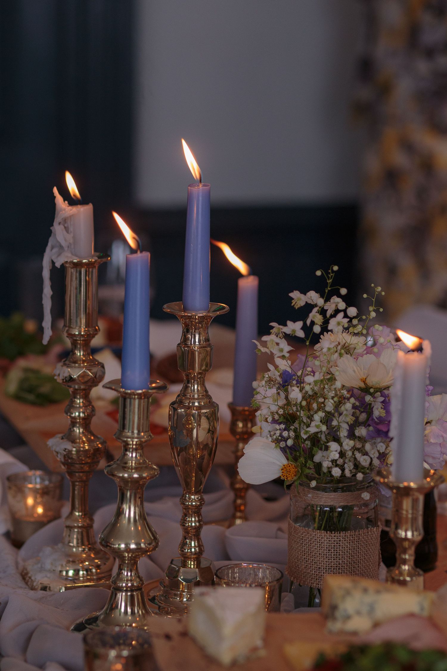 Wedding table décor. Gold candlesticks, blue candles burning away, bunches of baby's breath, and a selection of cheeses.