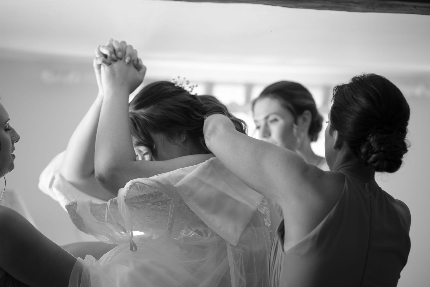 Black and White photos of three bridesmaids helping to get the wedding dress over the brides head