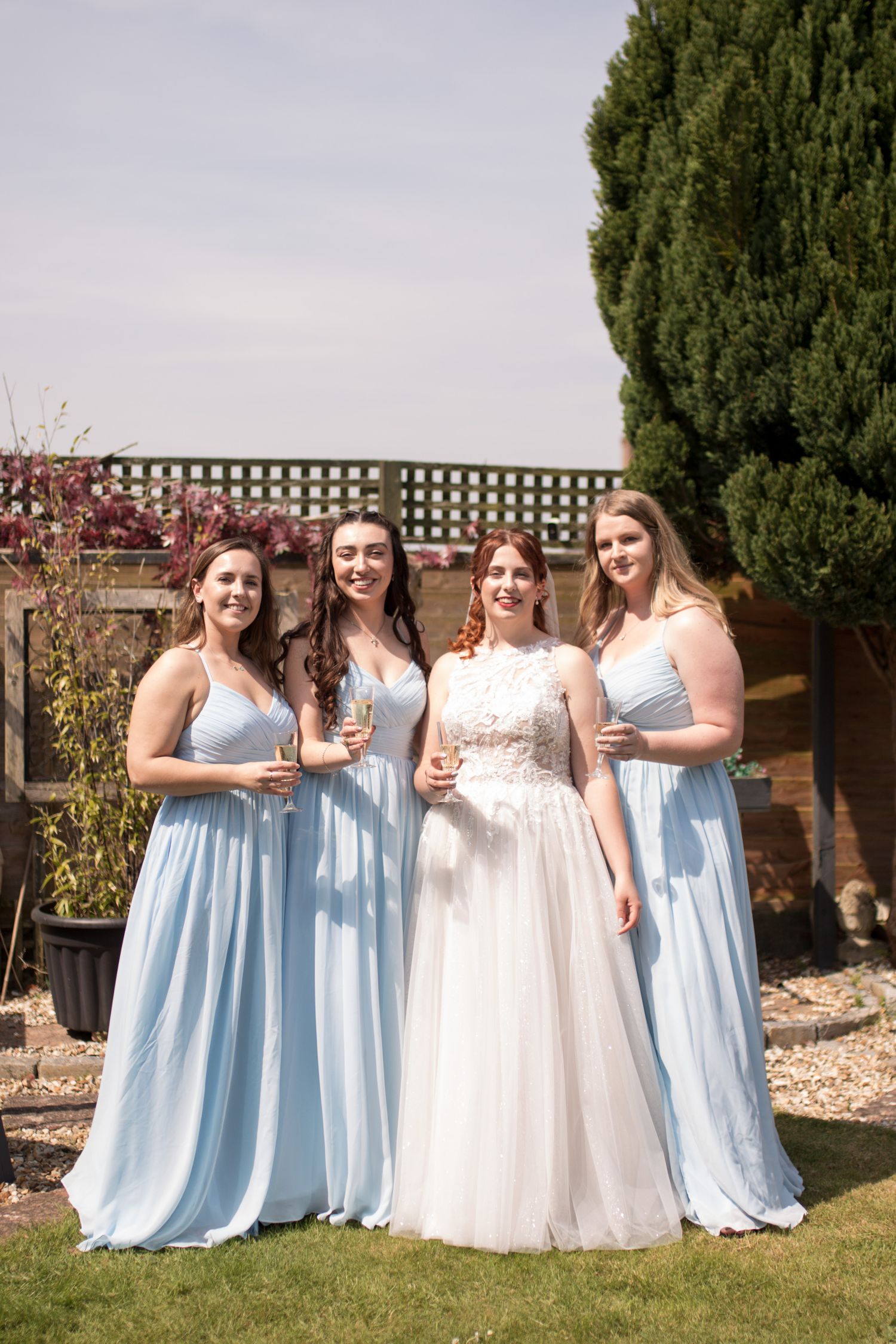 Bride and her three Bridesmaids pose for group photo in the garden before the ceremony, holding a glass of prosecco each.