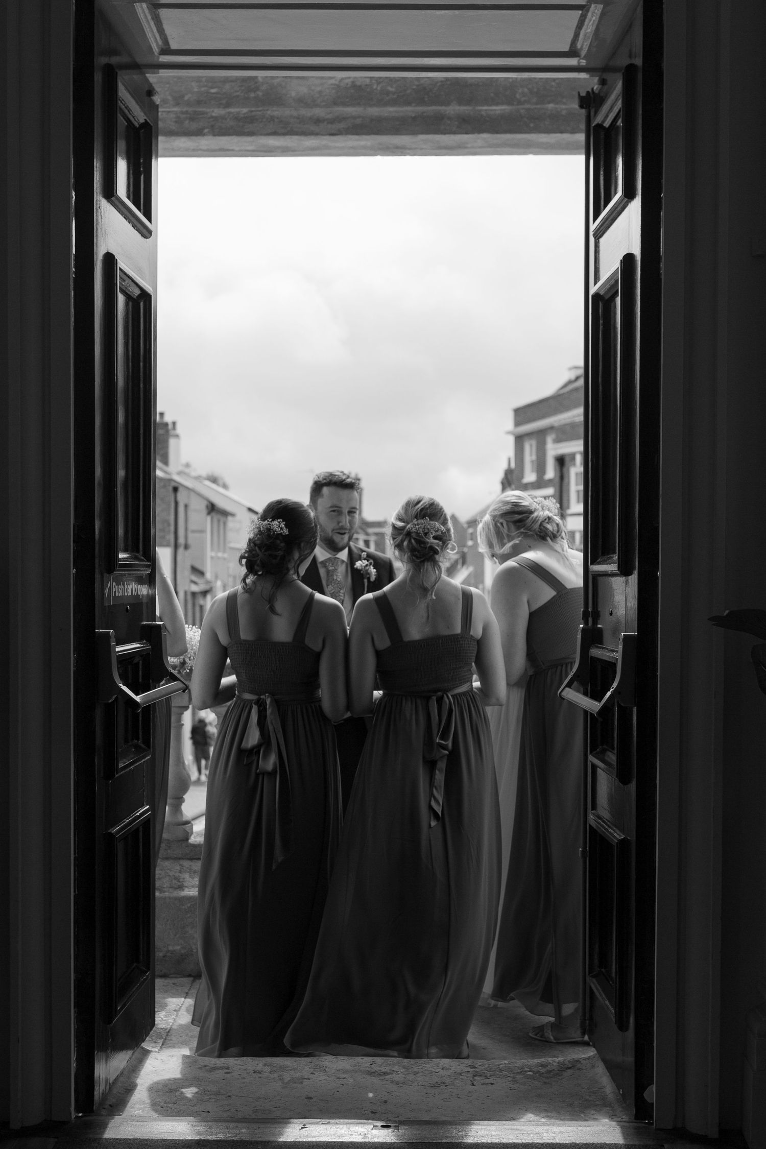 Groom stands talking to his sisters and other bridesmaids in the doorway of the Guildhall in Poole