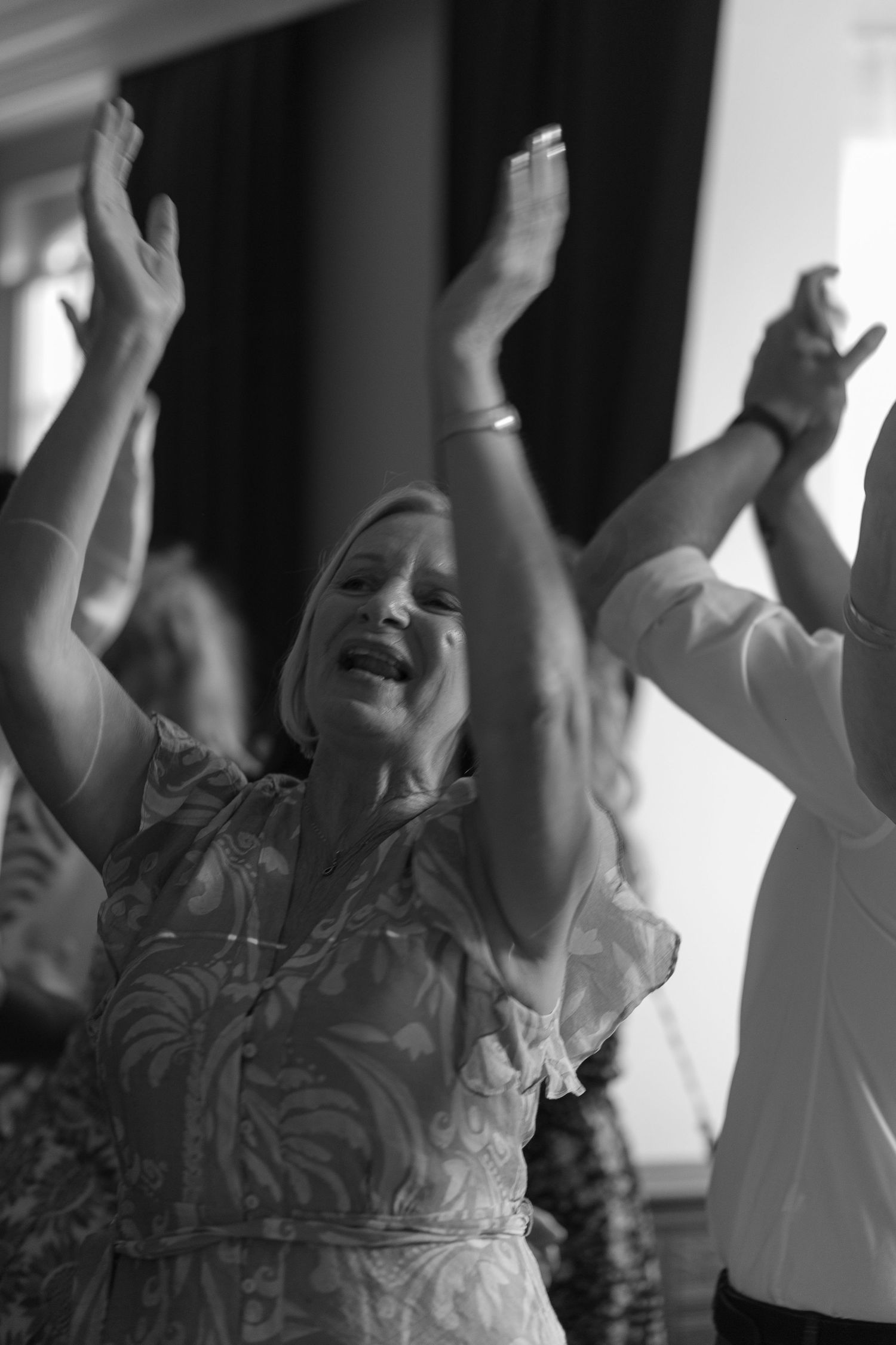 A black and white photo of a woman on the dance floor, lost in the music, her hands raised in the air.
