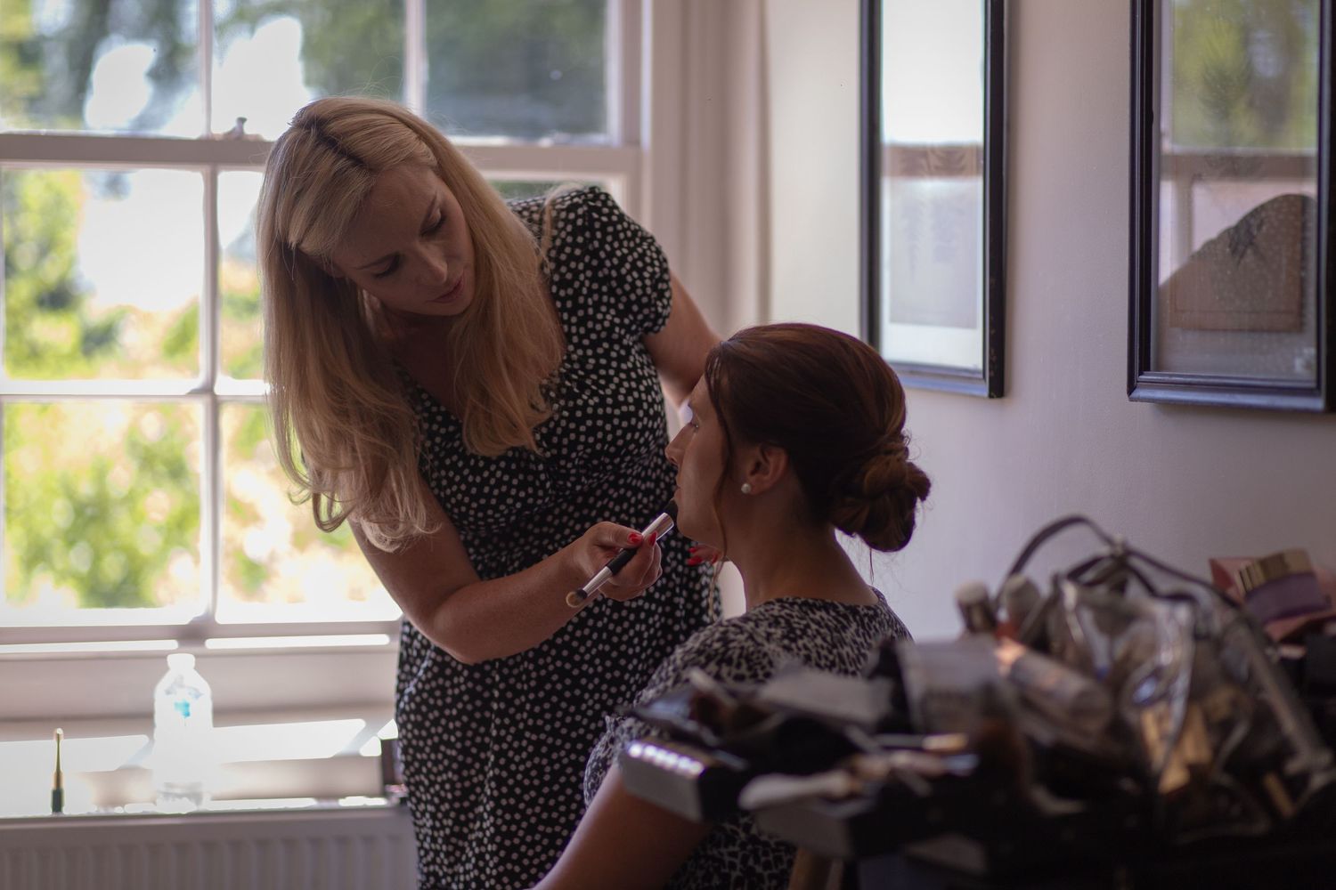 Make Up artist doing the make up of a bridesmaid surrounded by makeup brushes.