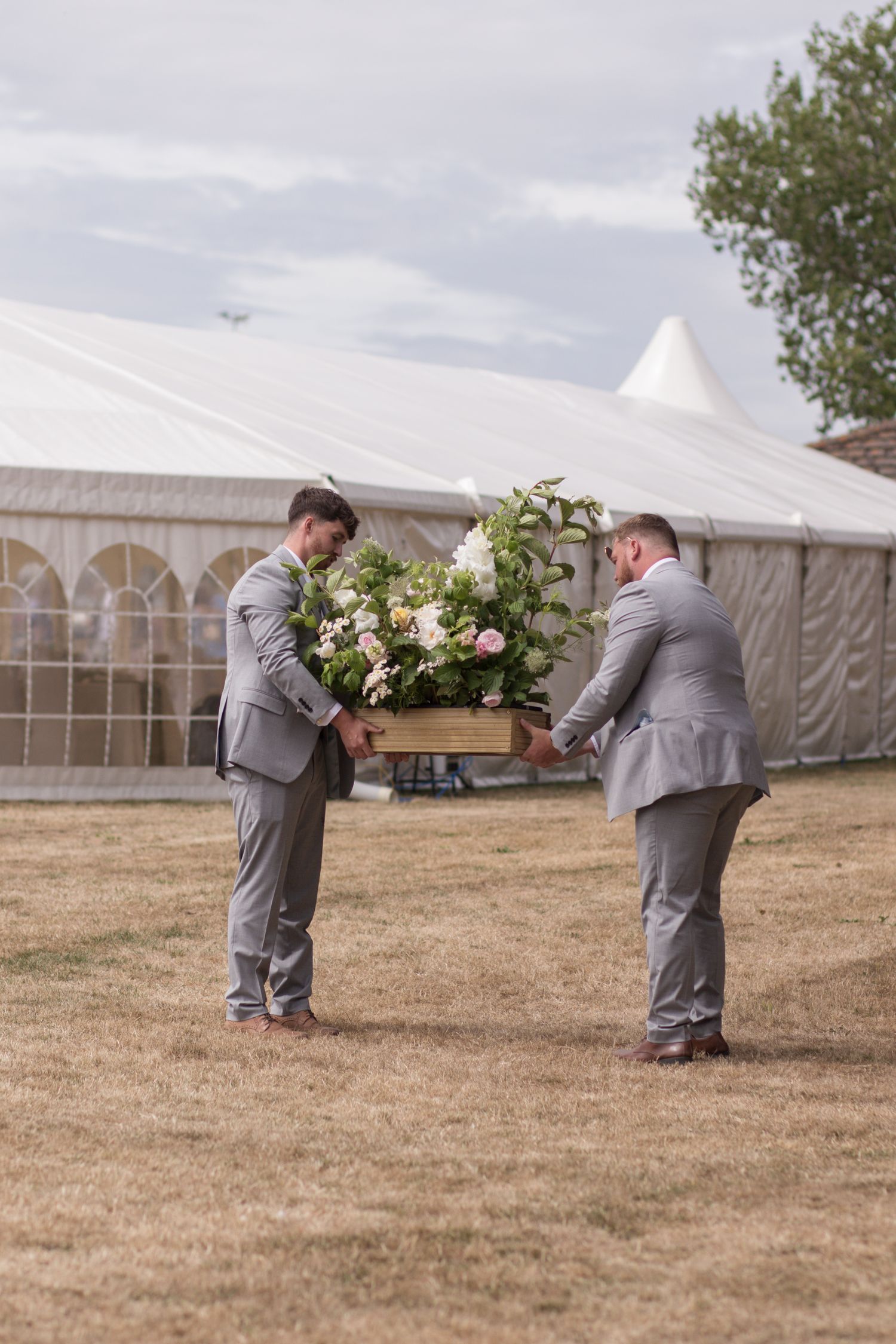 Two groomsmen carrying a floral display from the ceremony area into the evening marquee.