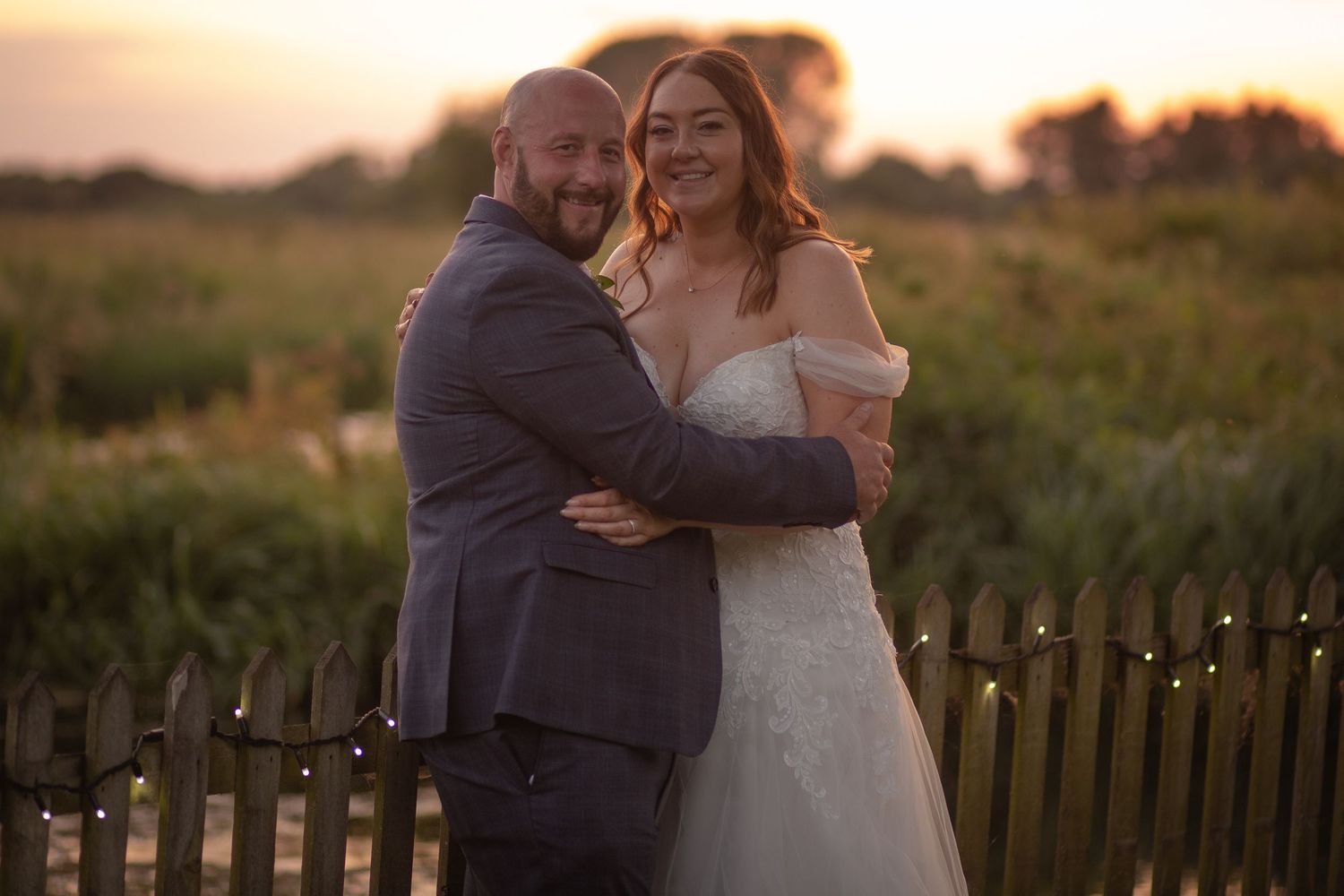Bride and Groom stand in an embrace facing the camera during sunset, with marsh lands and a river running behind them.