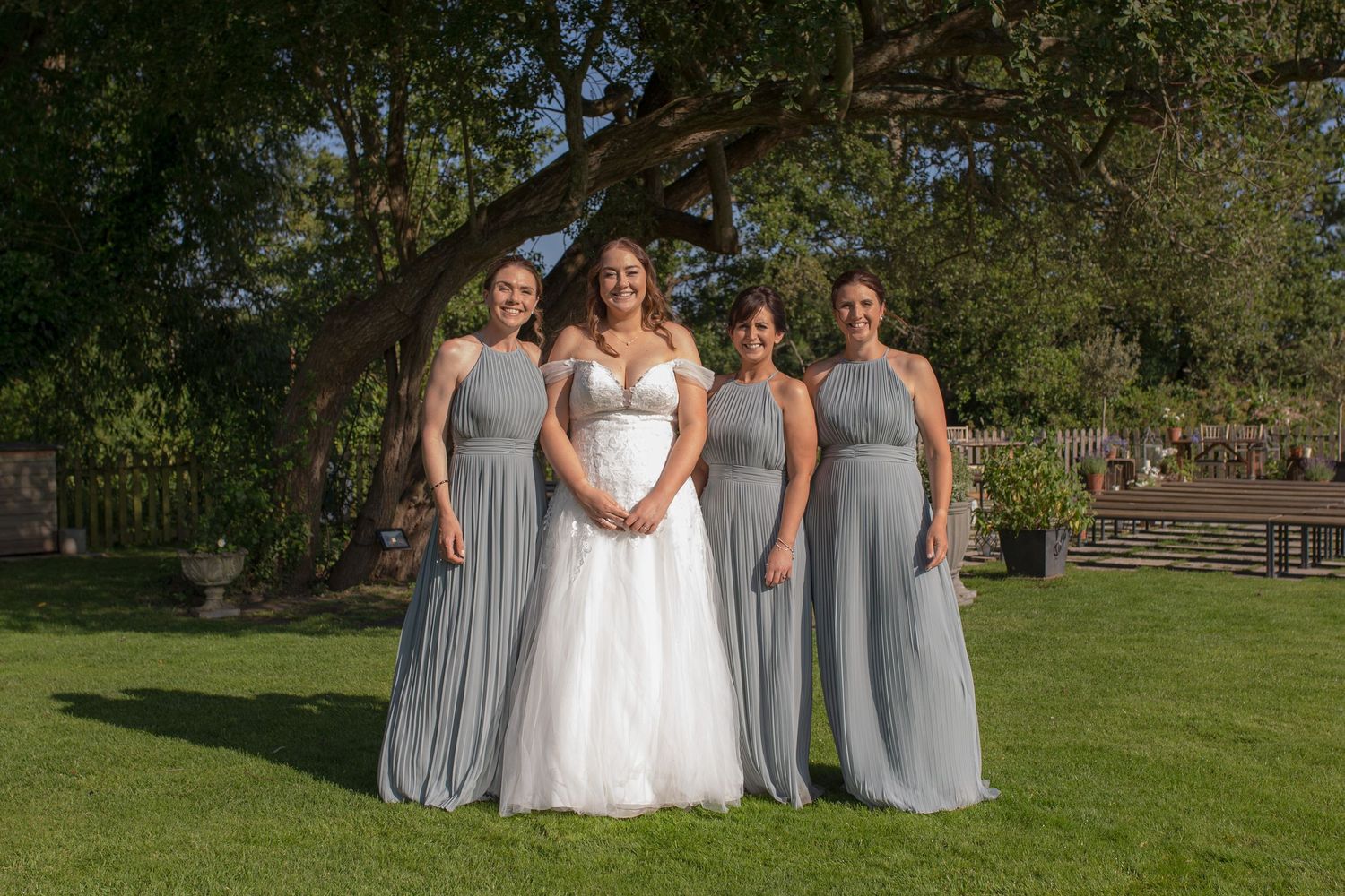 Bride and her three Bridesmaid pose for a photo in the gardens of Sopley Mill. The bride wears white, and the bridesmaids wear sage green