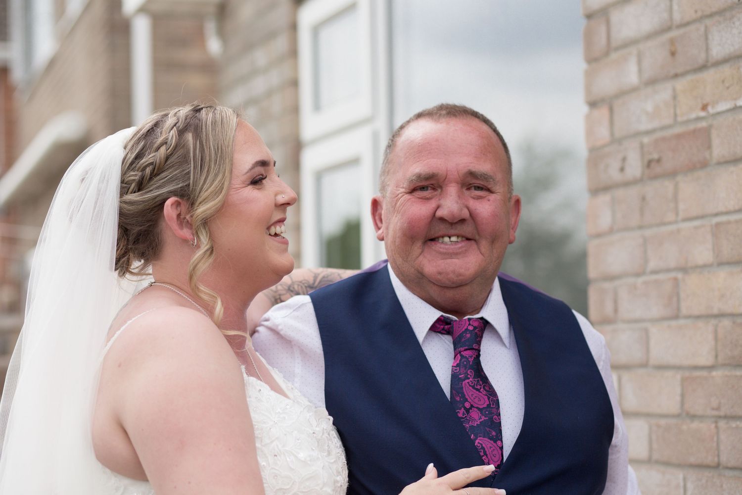 A bride and her dad together before the ceremony. Her dad smiles through his tears, whilst the bride laughs looking towards him.
