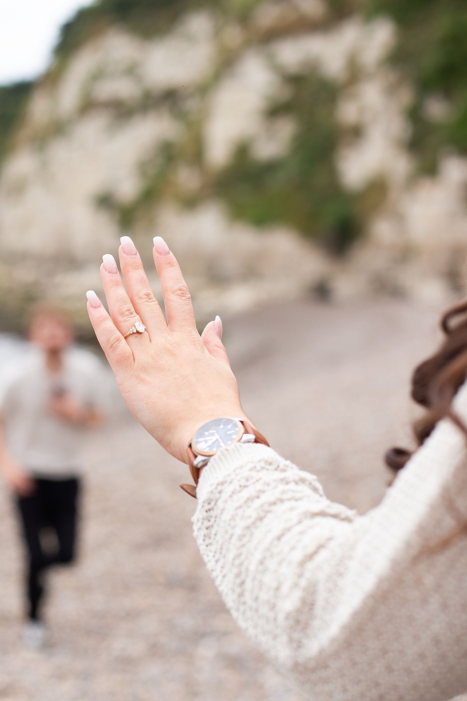 Woman's left hand, showing off her brand new engagement ring on a pebble beach after a proposal