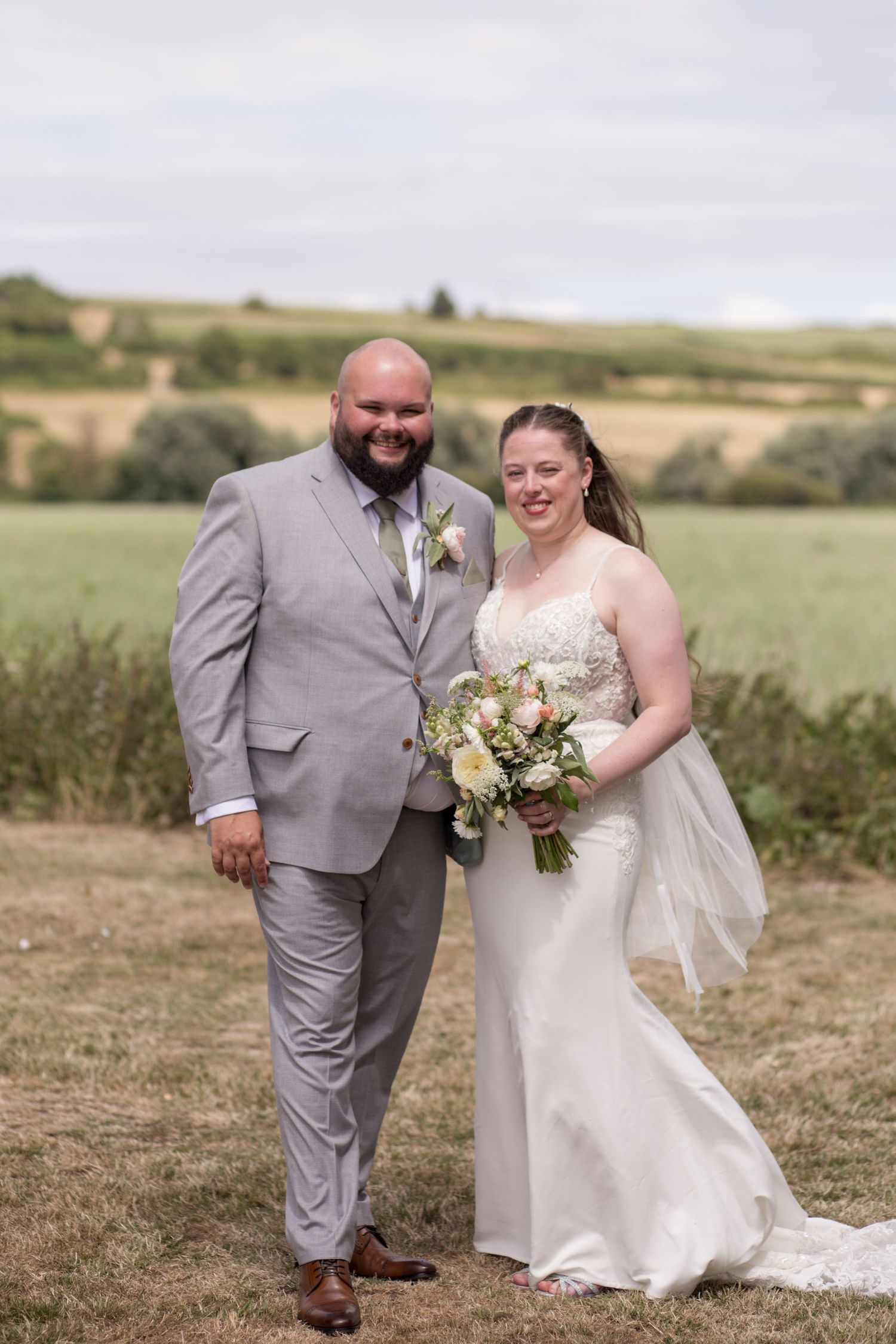 Bride and groom stood together smiling surrounded by rolling hills and fields.