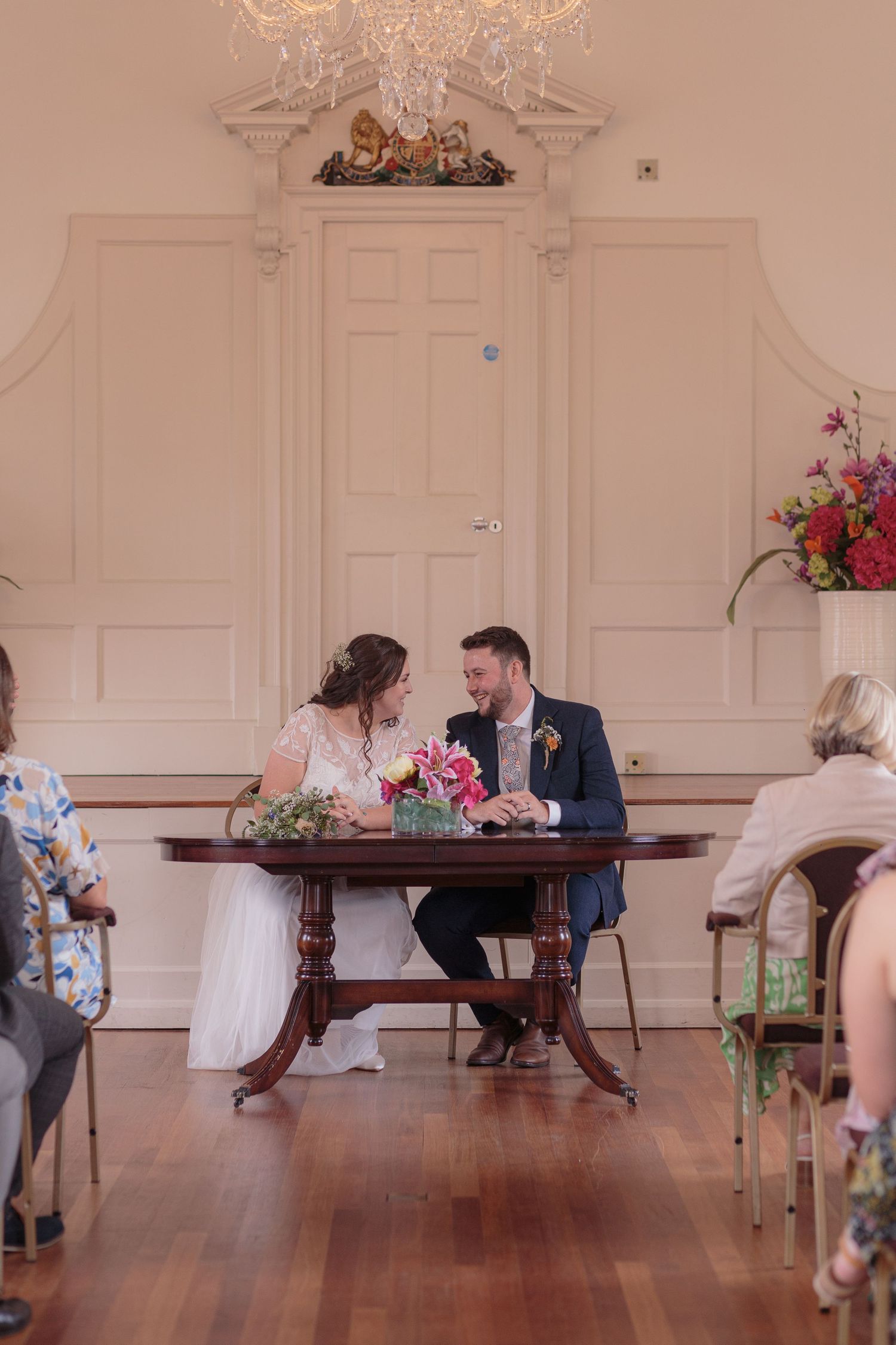 Bride and groom laugh together as they sit at a table to sign their marriage certificate