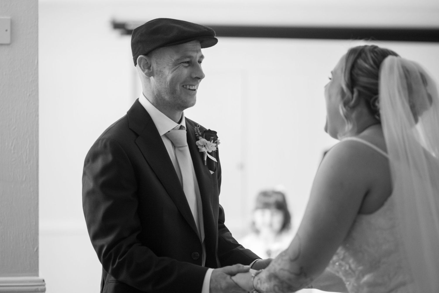 Bride and Groom stood holding hands during their ceremony. The Groom smiles at his bride, as she laughs back at him