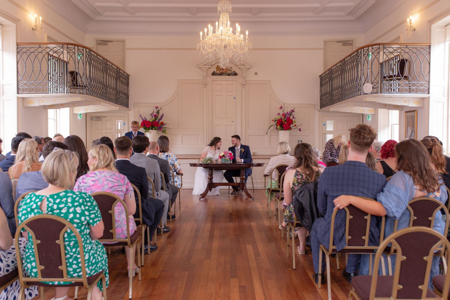 Friends and Family seen from behind as they sit and watch Bride and Groom sign the register during a Wedding Ceremony at Poole Guildhall
