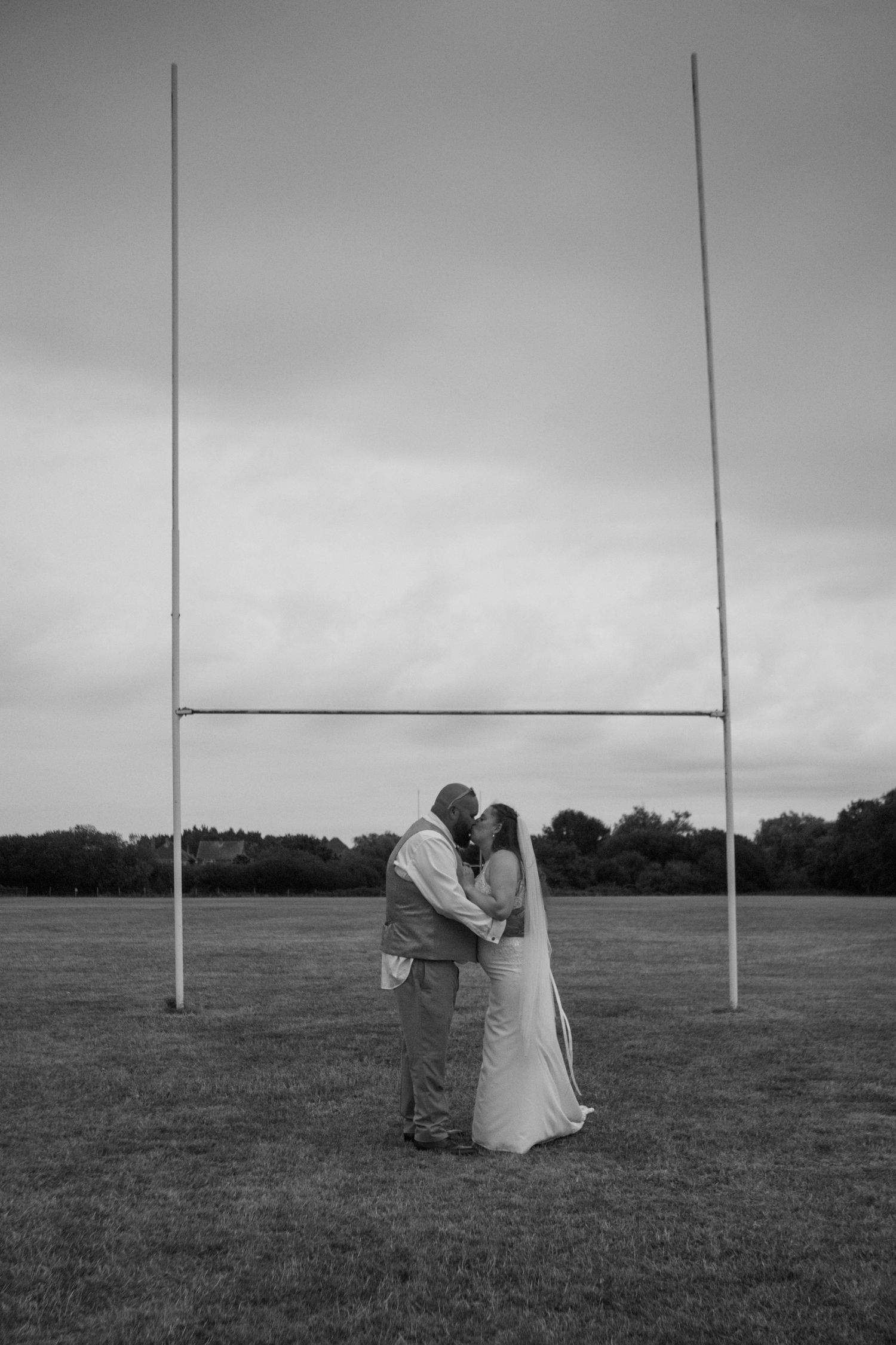Black and White photo of a Bride and Groom kissing underneath the Rugby posts