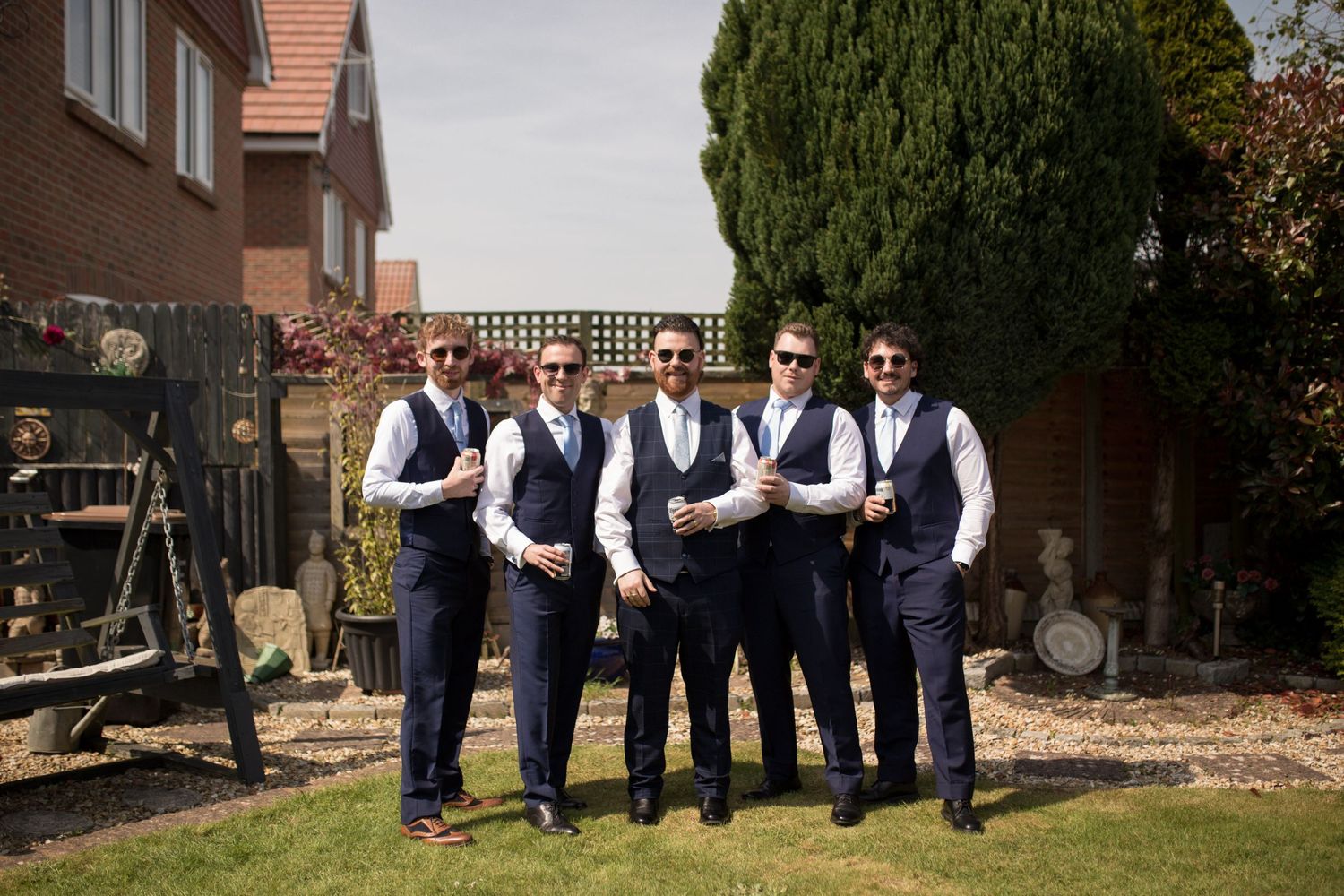 Groom and his four groomsmen in matching navy blue suits posing for a group photo in the garden before the ceremony.