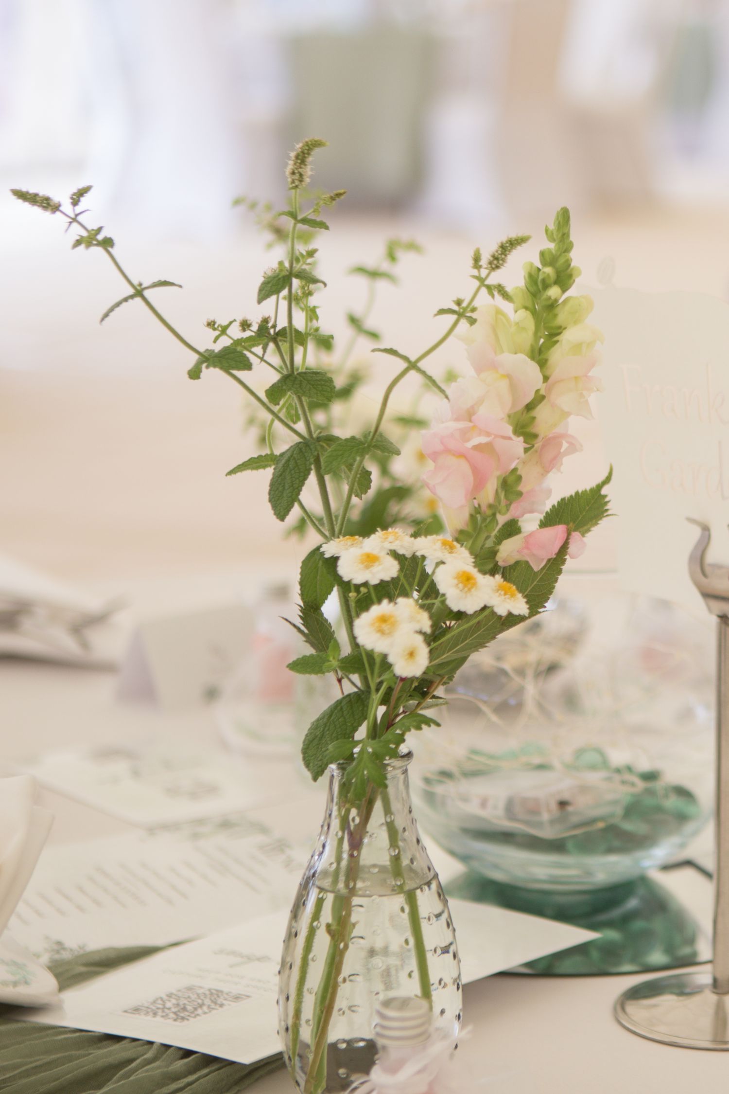 Delicate flower centrepieces. Flowers of pink and white, with lots of greenery in little bud vases.