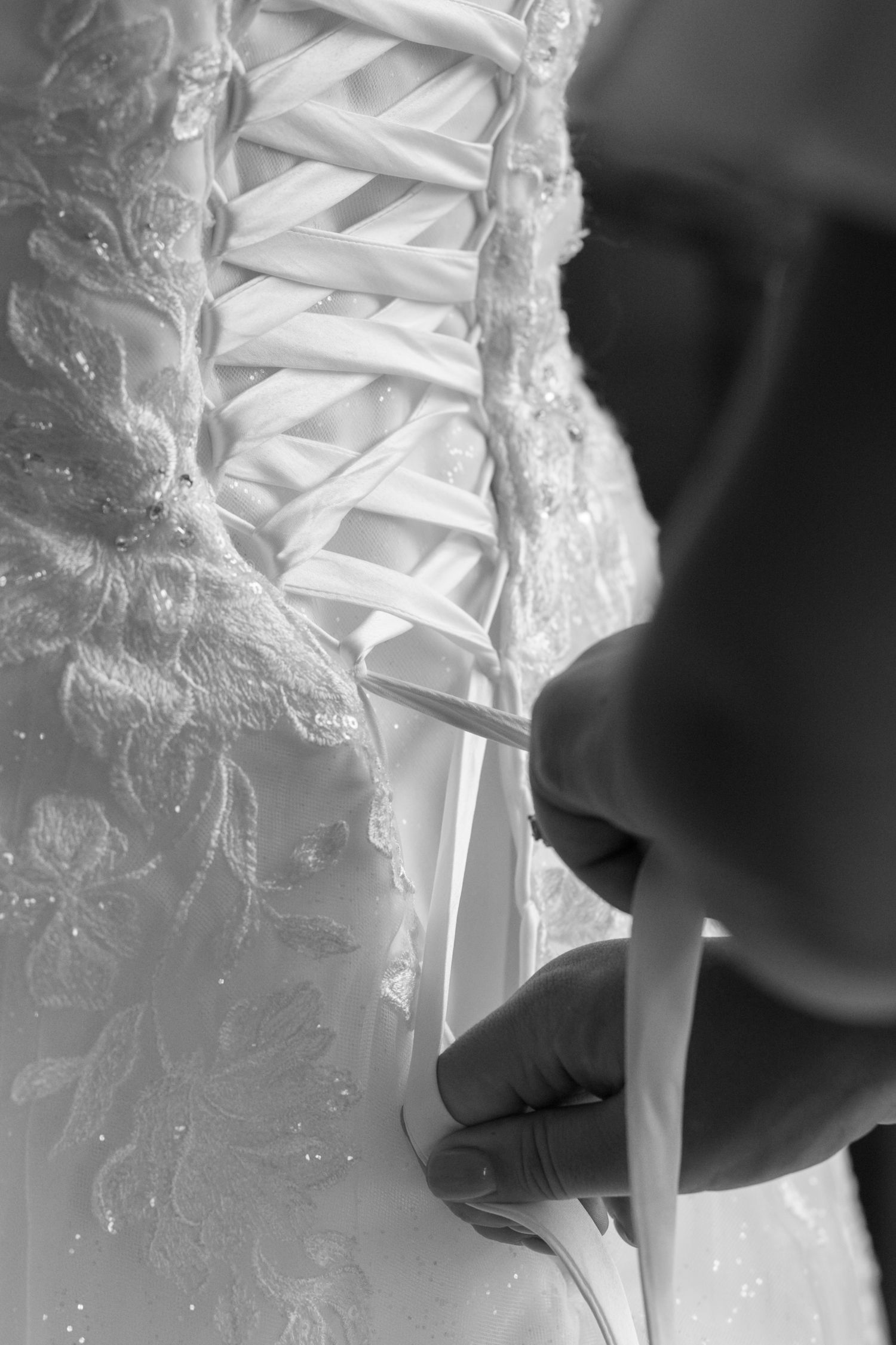 Close up of the back of the wedding dress, with a pair of hands lacing up the corset back