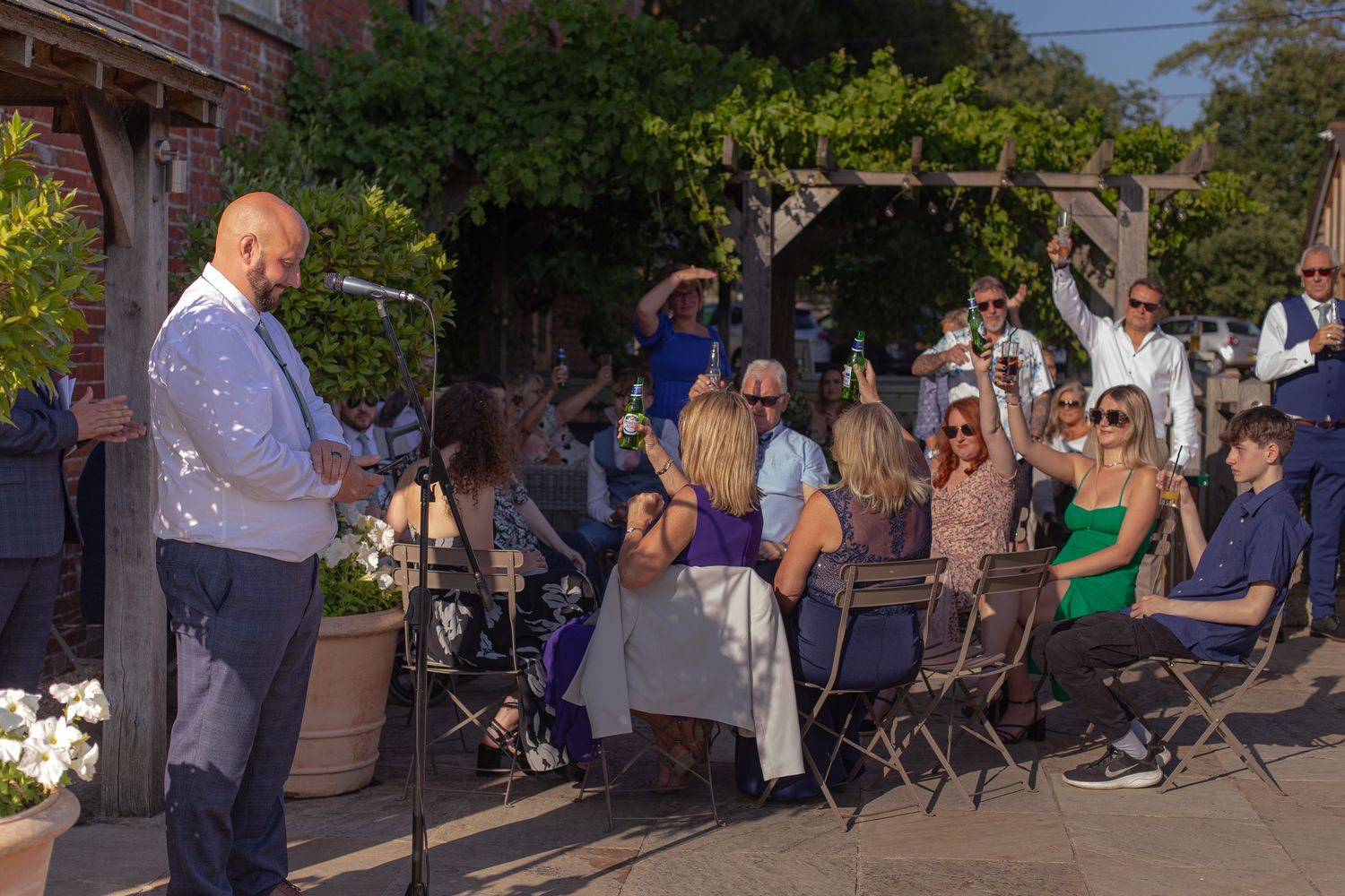 Wedding guests raise their drinks in a toast as the groom gives a speech