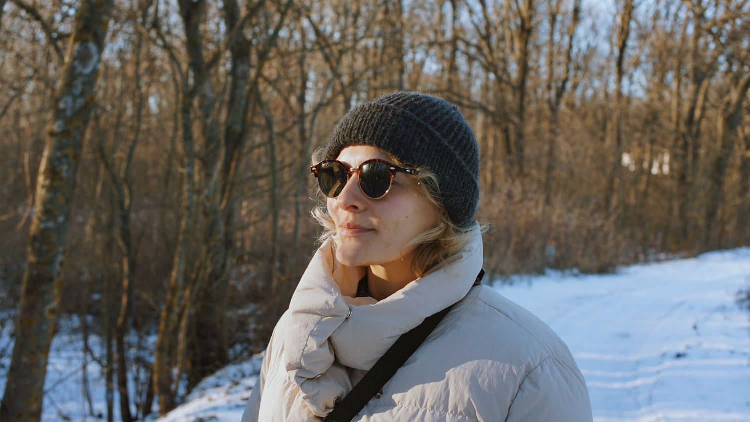 A snowy winter landscape with bare trees and a person wearing sunglasses and winter clothing enjoying the outdoors.