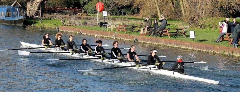 Rowing teams competing on river with boats lined up in formation.
