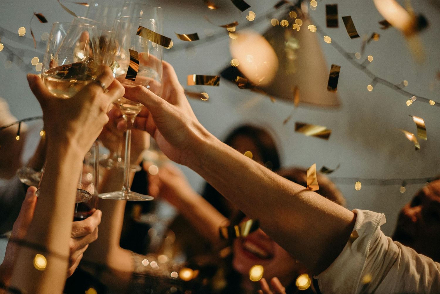 Hands raise champagne glasses in celebration as golden confetti falls through the air.