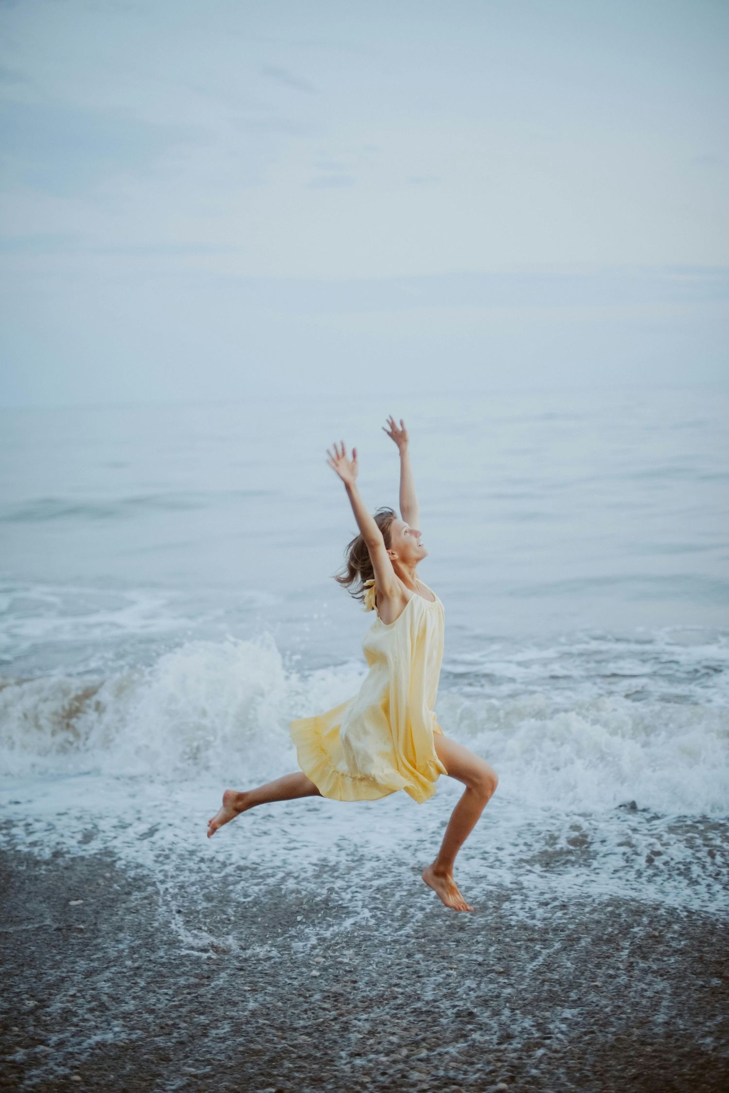 Figure in yellow dress dancing and jumping on a misty beach.
