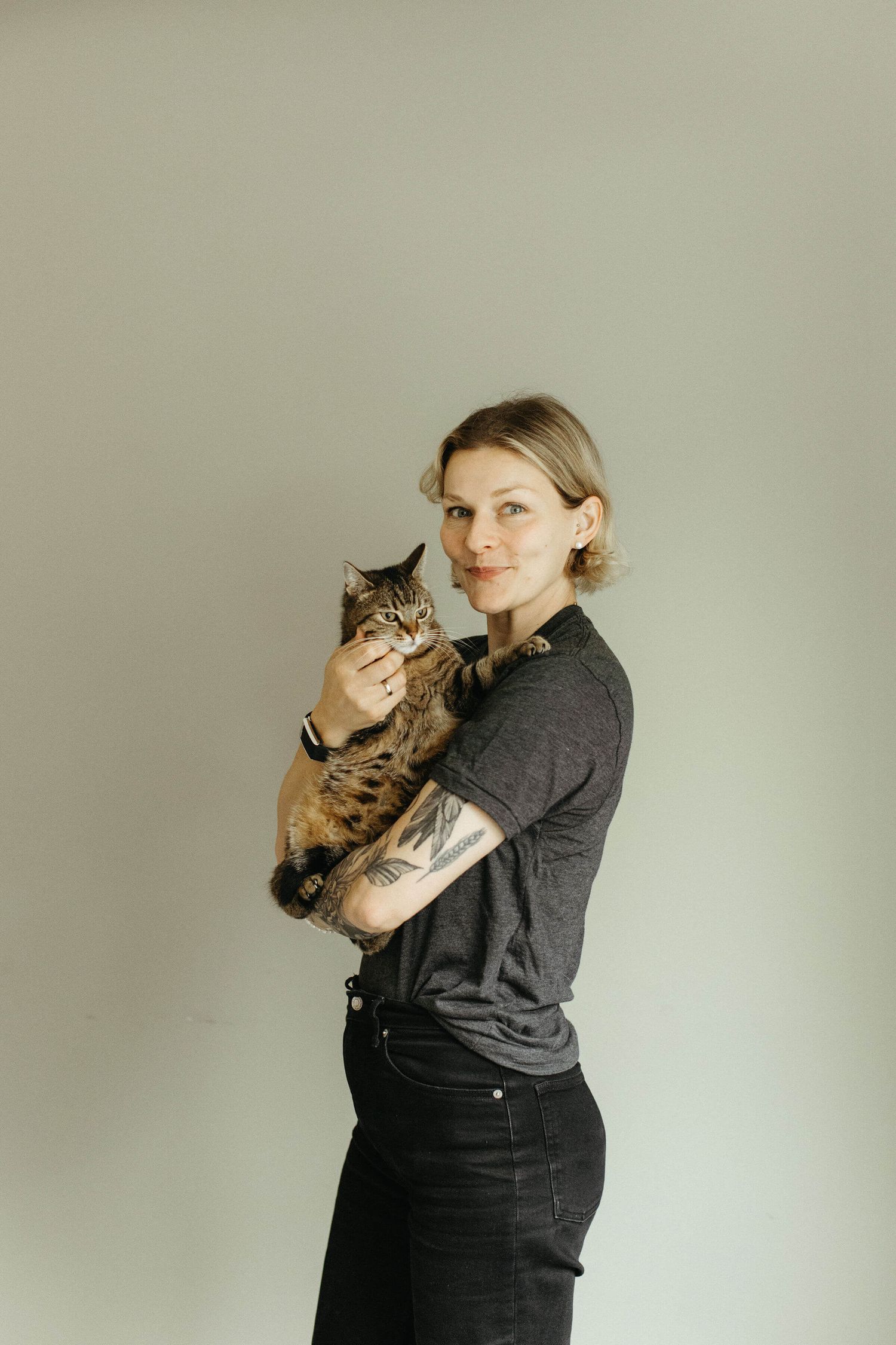 Person in dark clothing holding and posing with a striped tabby cat in multiple shots.