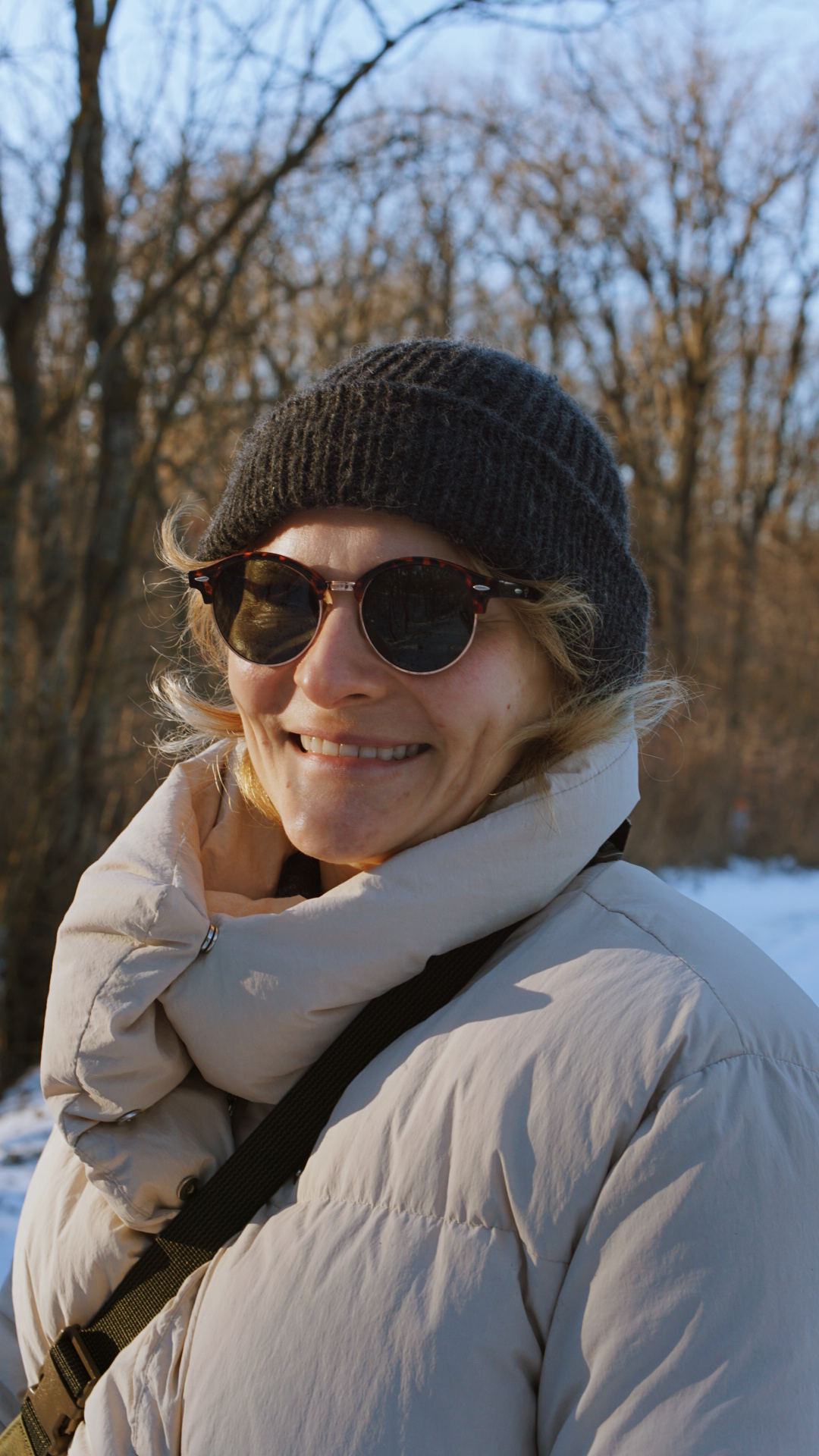 Someone wearing a white winter coat and knit beanie smiles while enjoying a sunny winter day.
