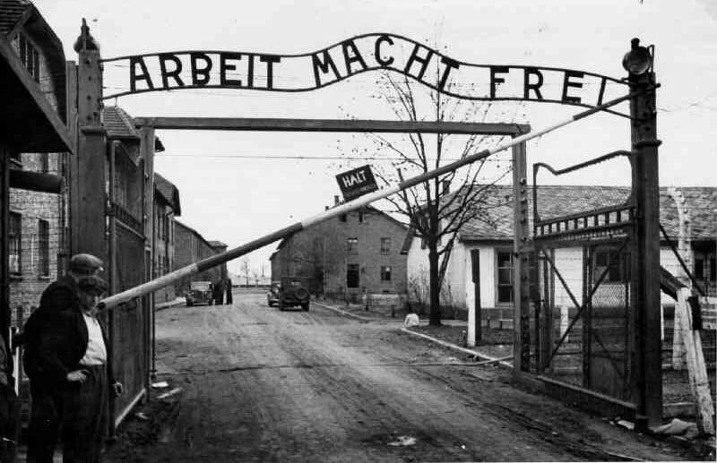 Historic entrance gate to Auschwitz concentration camp with infamous 'Arbeit Macht Frei' sign overhead.