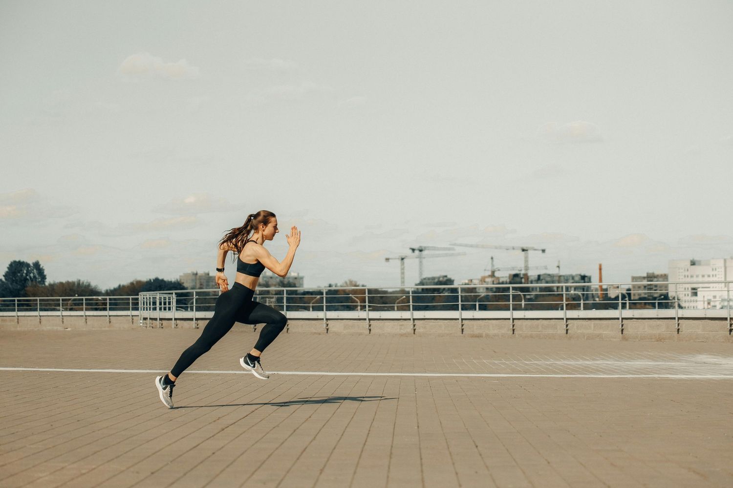 Athletic person sprinting on an empty rooftop against an urban backdrop.