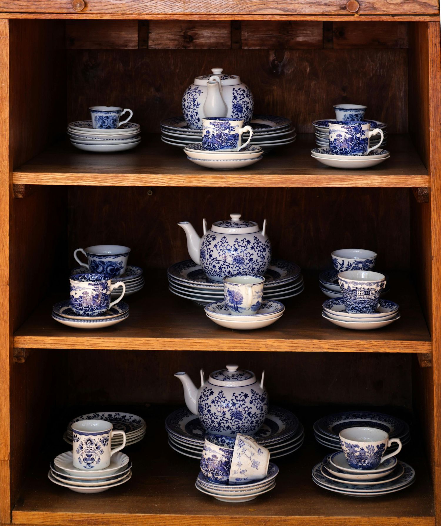 Wooden shelving unit displaying blue and white porcelain tea sets and dishes.