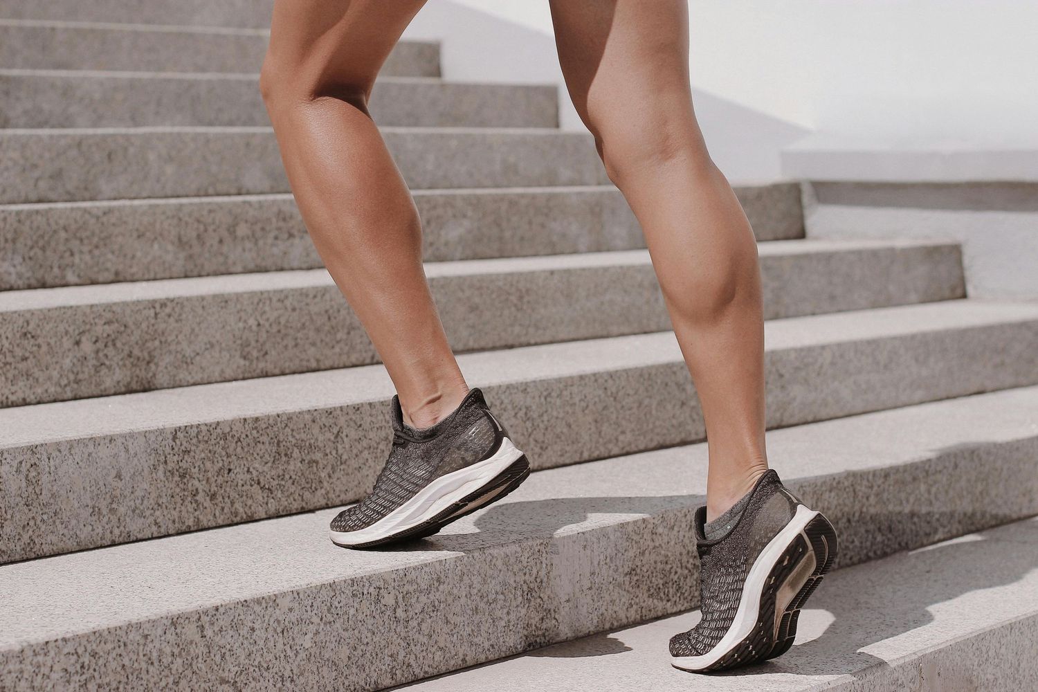 Close-up of athletic legs in sneakers climbing concrete stairs.