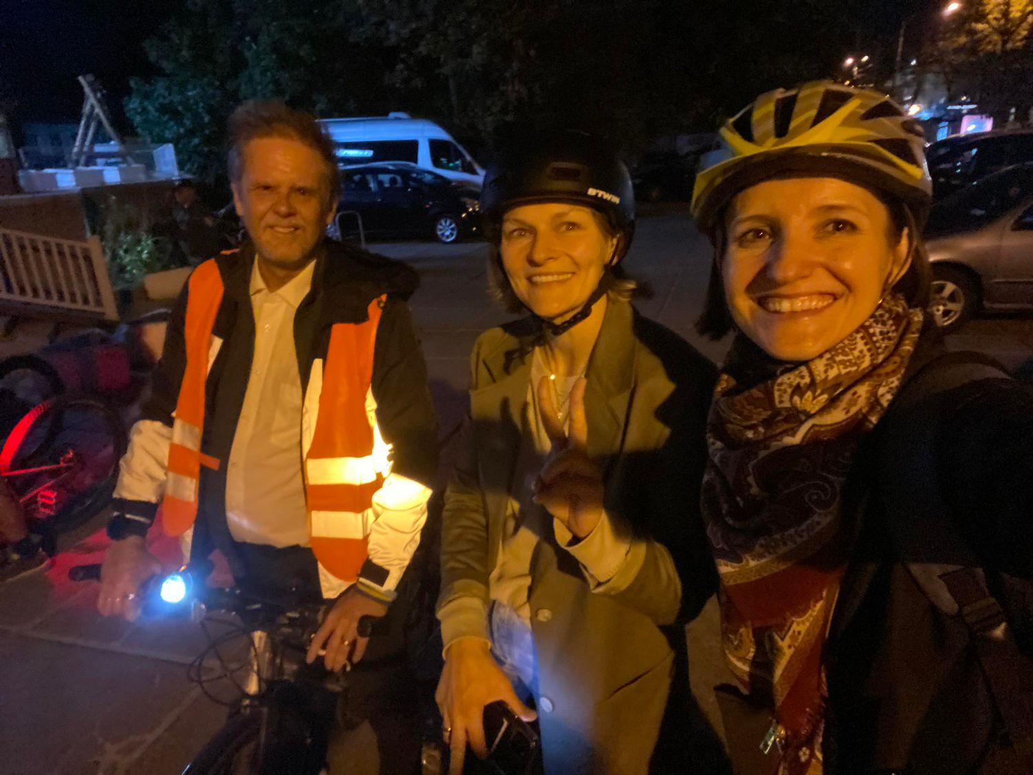 Three cyclists in safety gear holding lights gather at night for a bike ride.